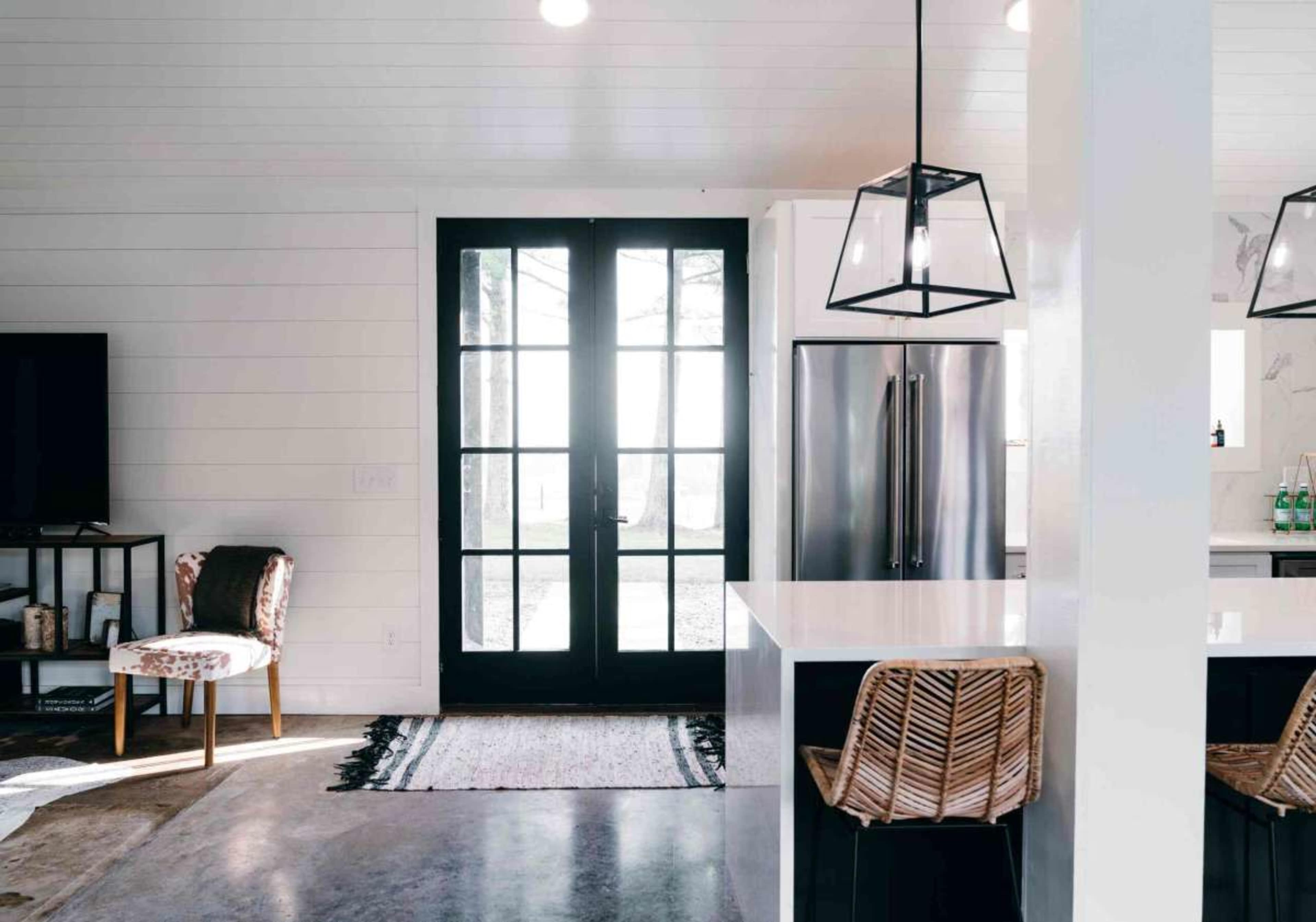 The image shows a modern kitchen with a central island, stainless steel appliances, and a black door leading outside.