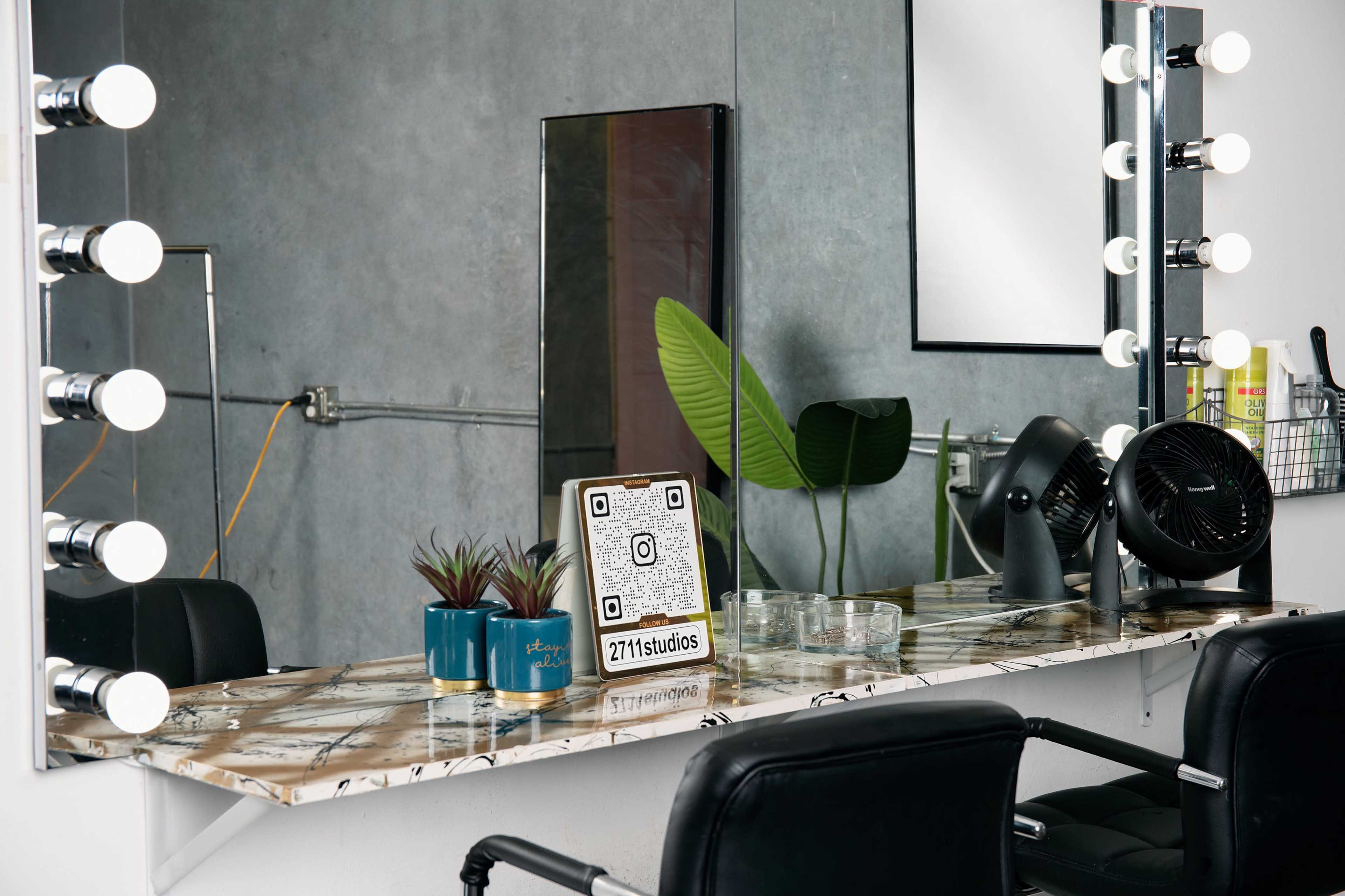A modern hair salon mirror with bright lights, a marble countertop, potted plants, and a small fan.