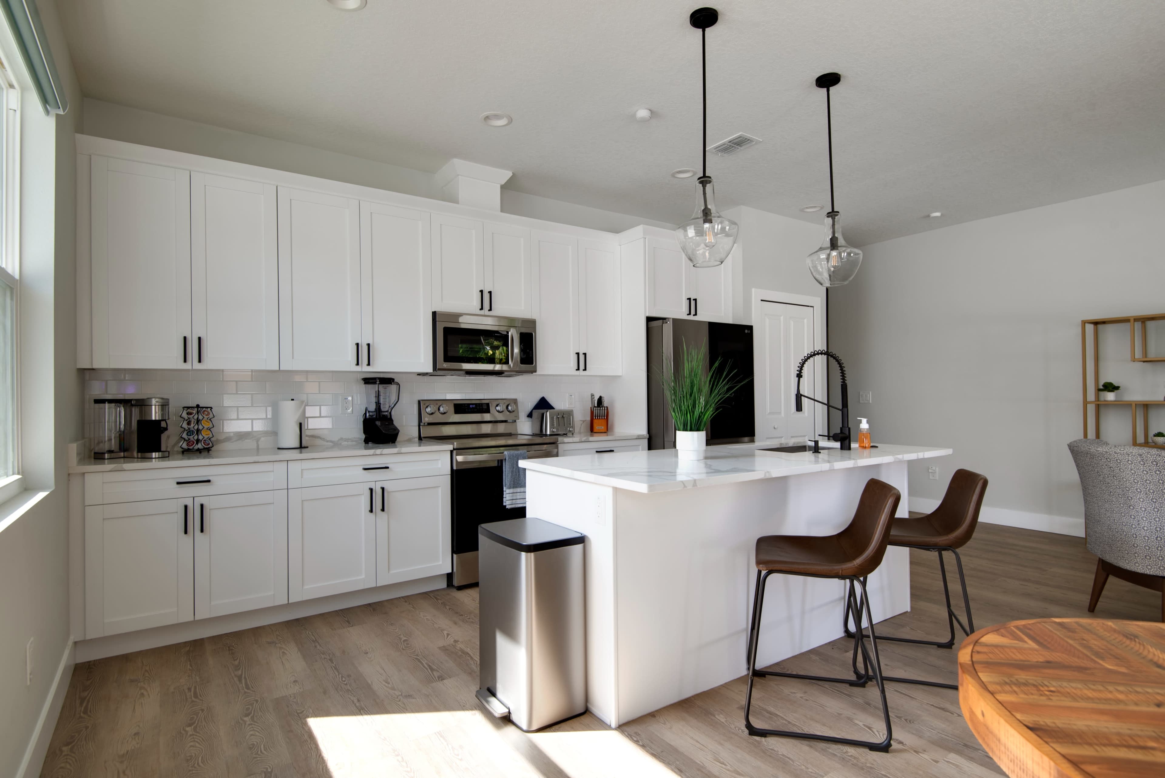 A modern kitchen features white cabinets, stainless steel appliances, and a large island with bar stools.