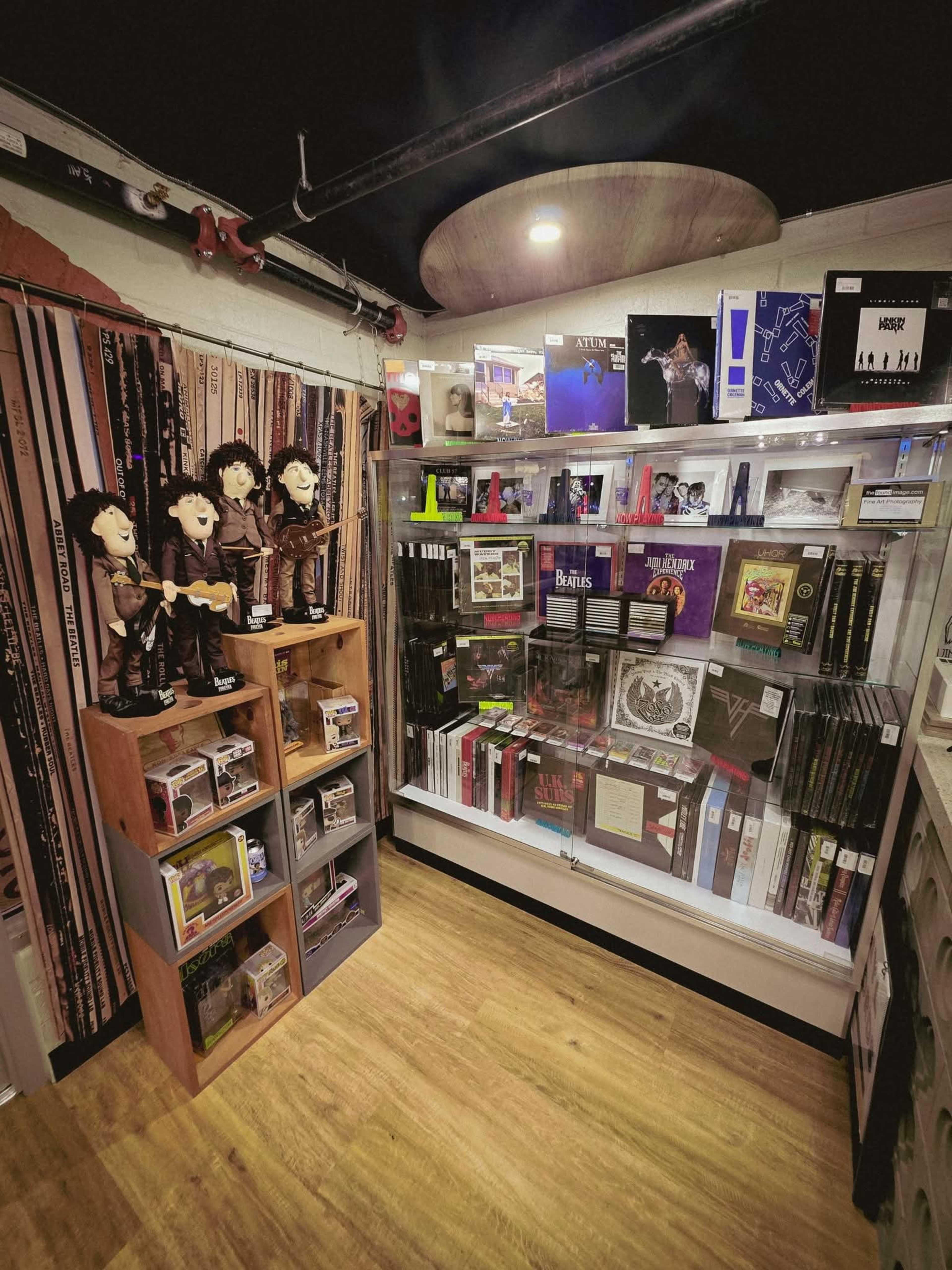 The image shows a corner of a store displaying various music memorabilia, including figurines, albums, and collectibles arranged on shelves.