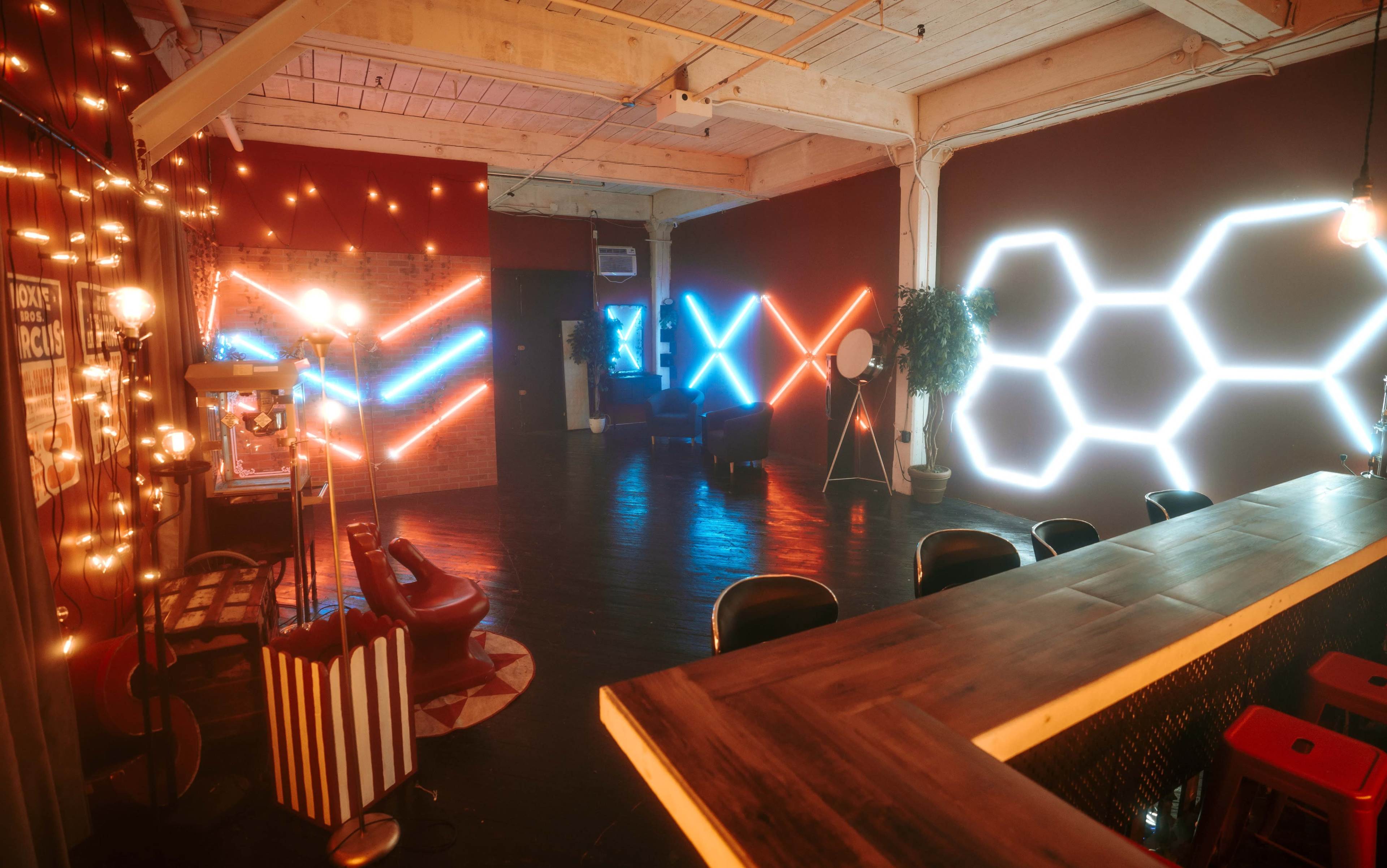 The image shows a modern interior space featuring illuminated wall designs in blue and red, a bar area, and stylish seating arranged around a rug.