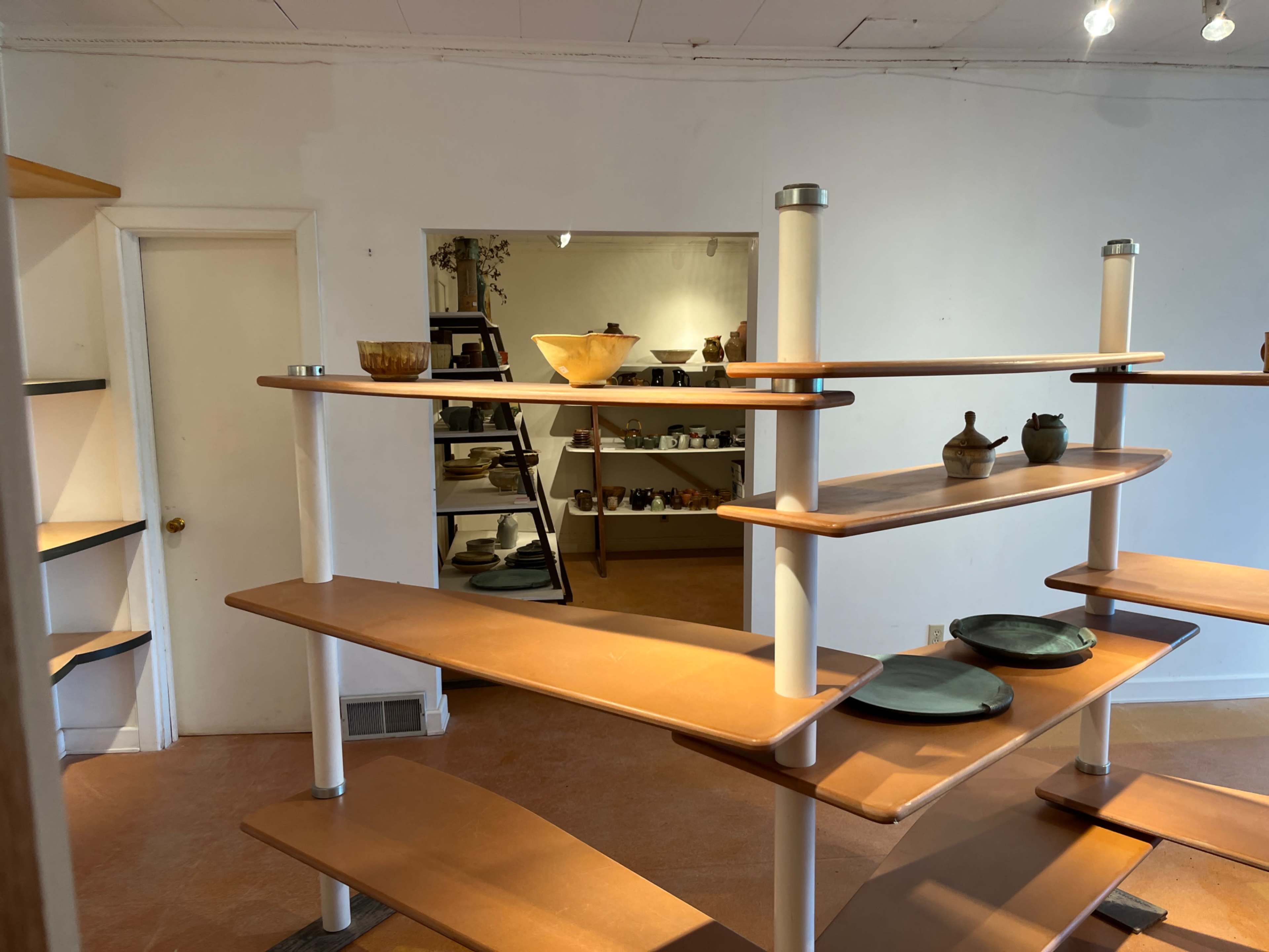 The image shows a spacious interior with wooden display shelves showcasing various ceramic dishware and bowls.