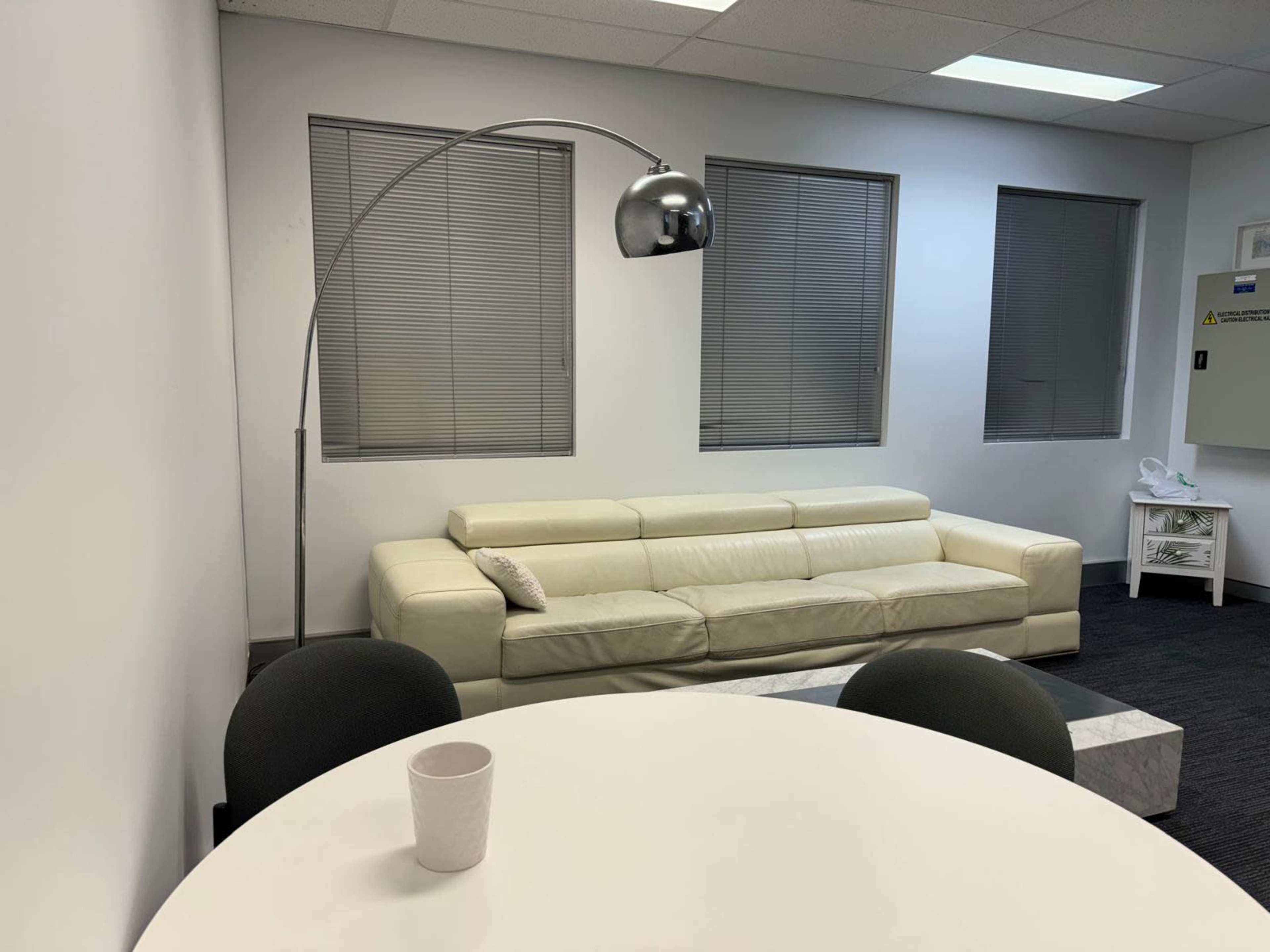 A modern office space with a white sofa, a round table, and a floor lamp.