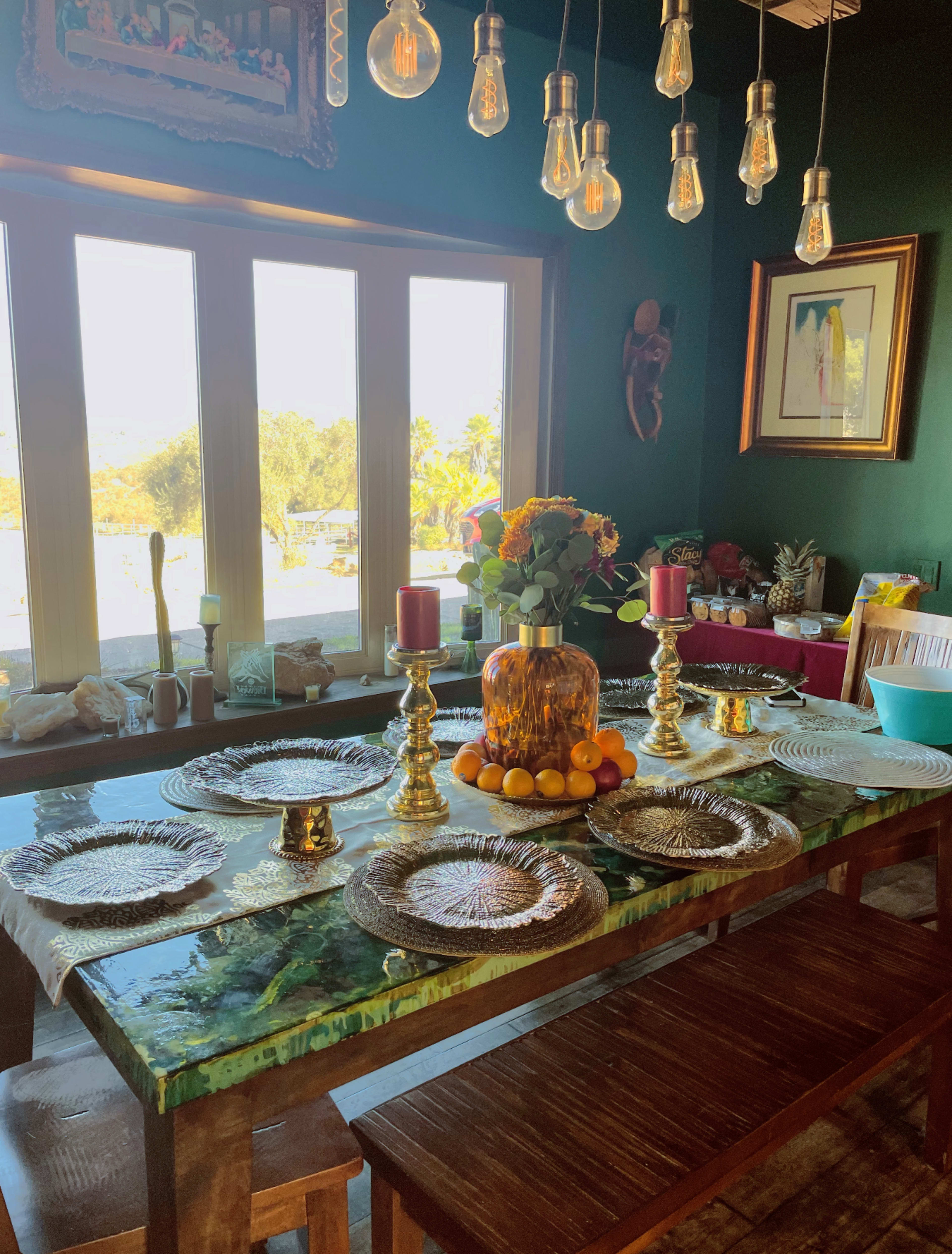 A dining table set with decorative plates and candle holders is arranged near a window, showcasing a view of the outdoors.