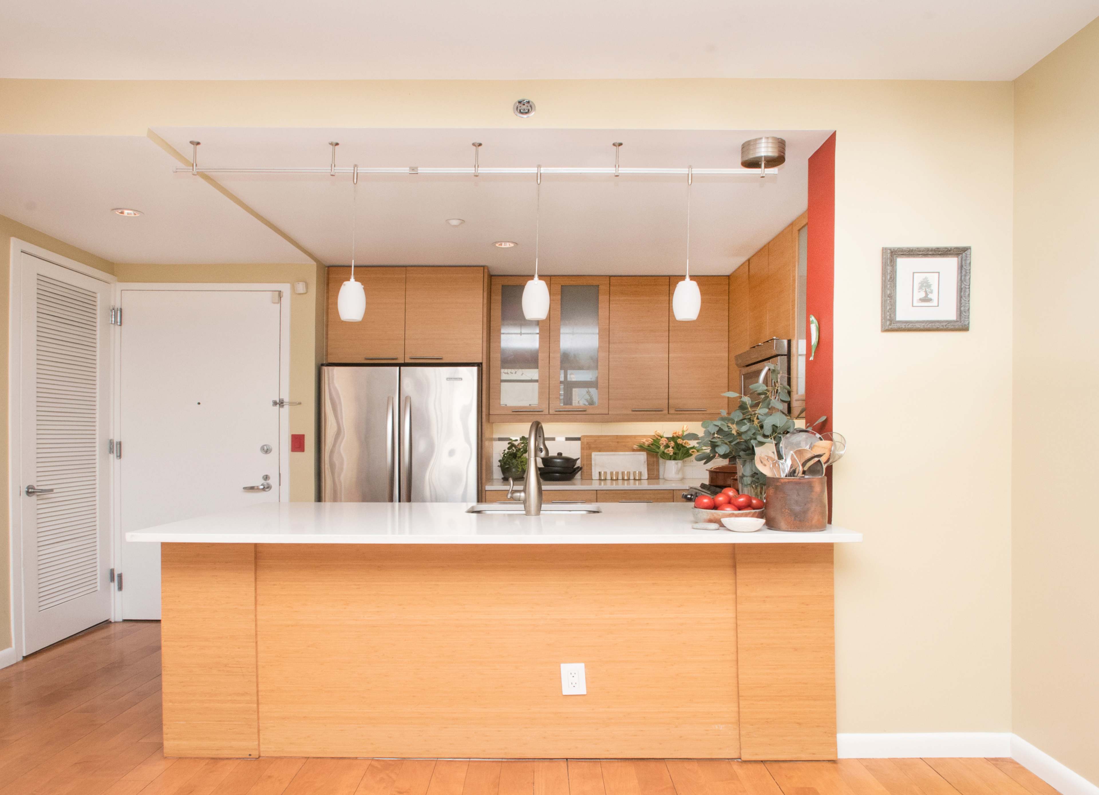 The image shows a modern kitchen with a sleek island, stainless steel appliances, and pendant lighting.