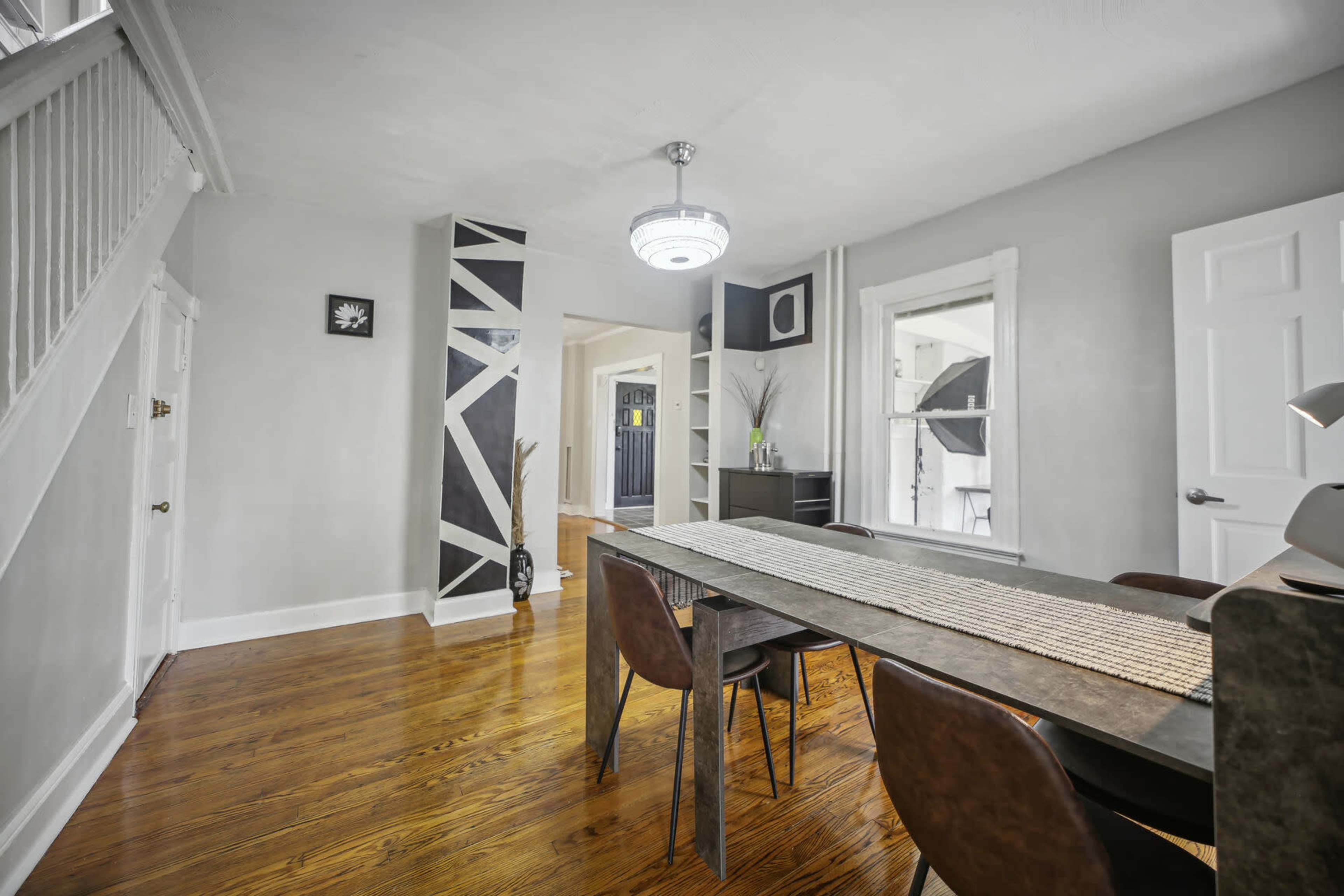 A dining area features a long table with chairs, a geometric accent wall, and a modern light fixture.