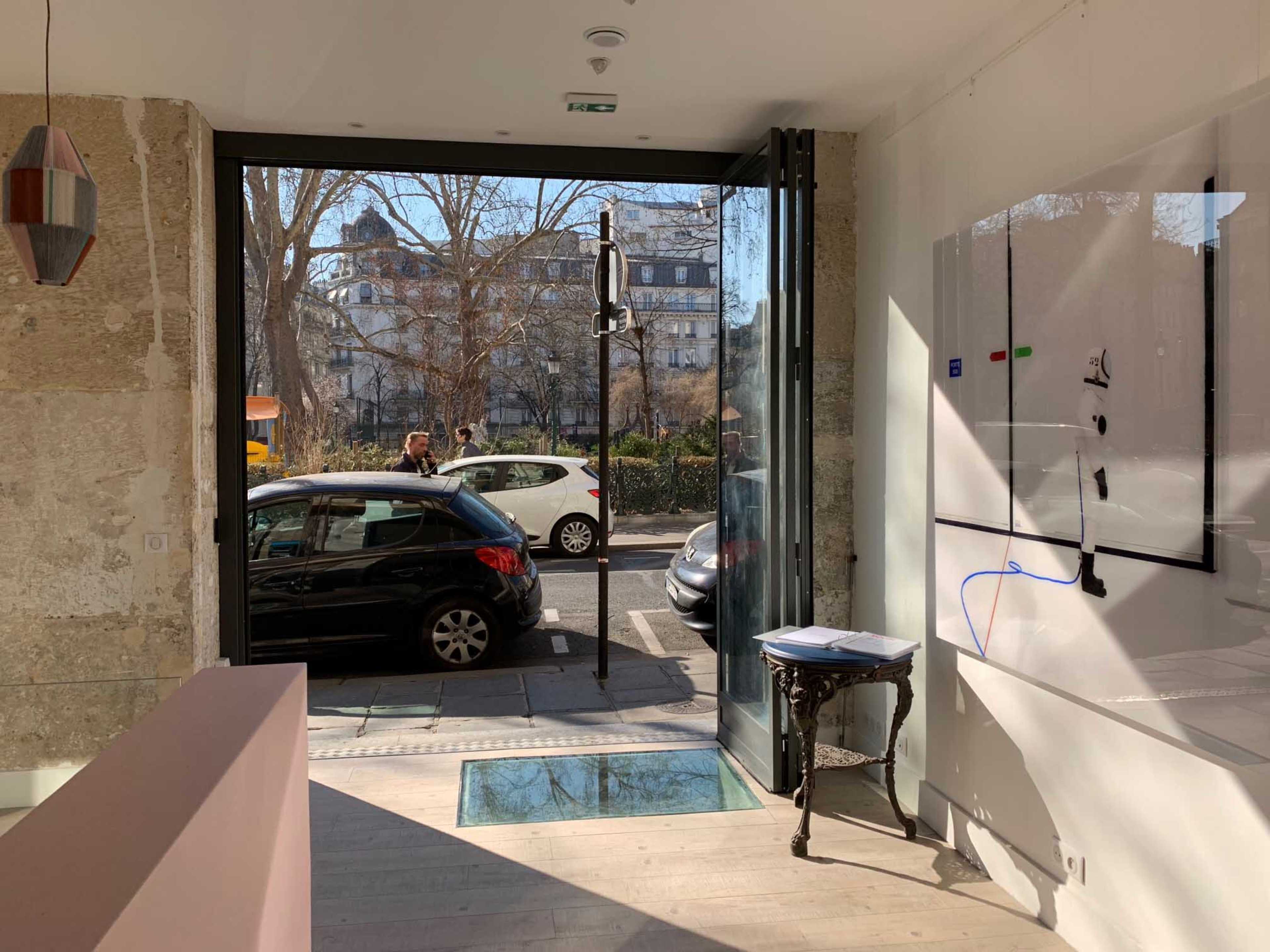 A large glass door opens to a street view, showcasing a car parked outside and a person walking by.