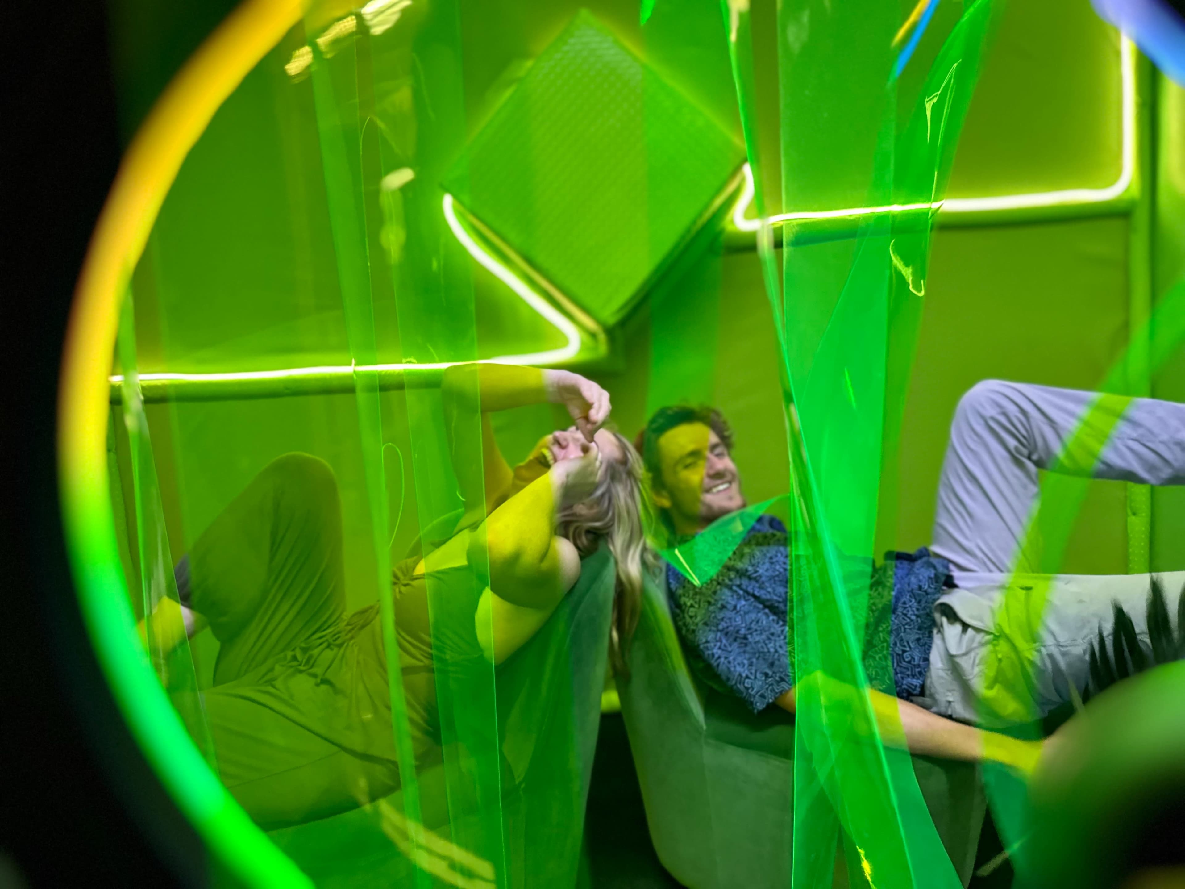 Two individuals relax on green couches inside an illuminated space with green translucent partitions.
