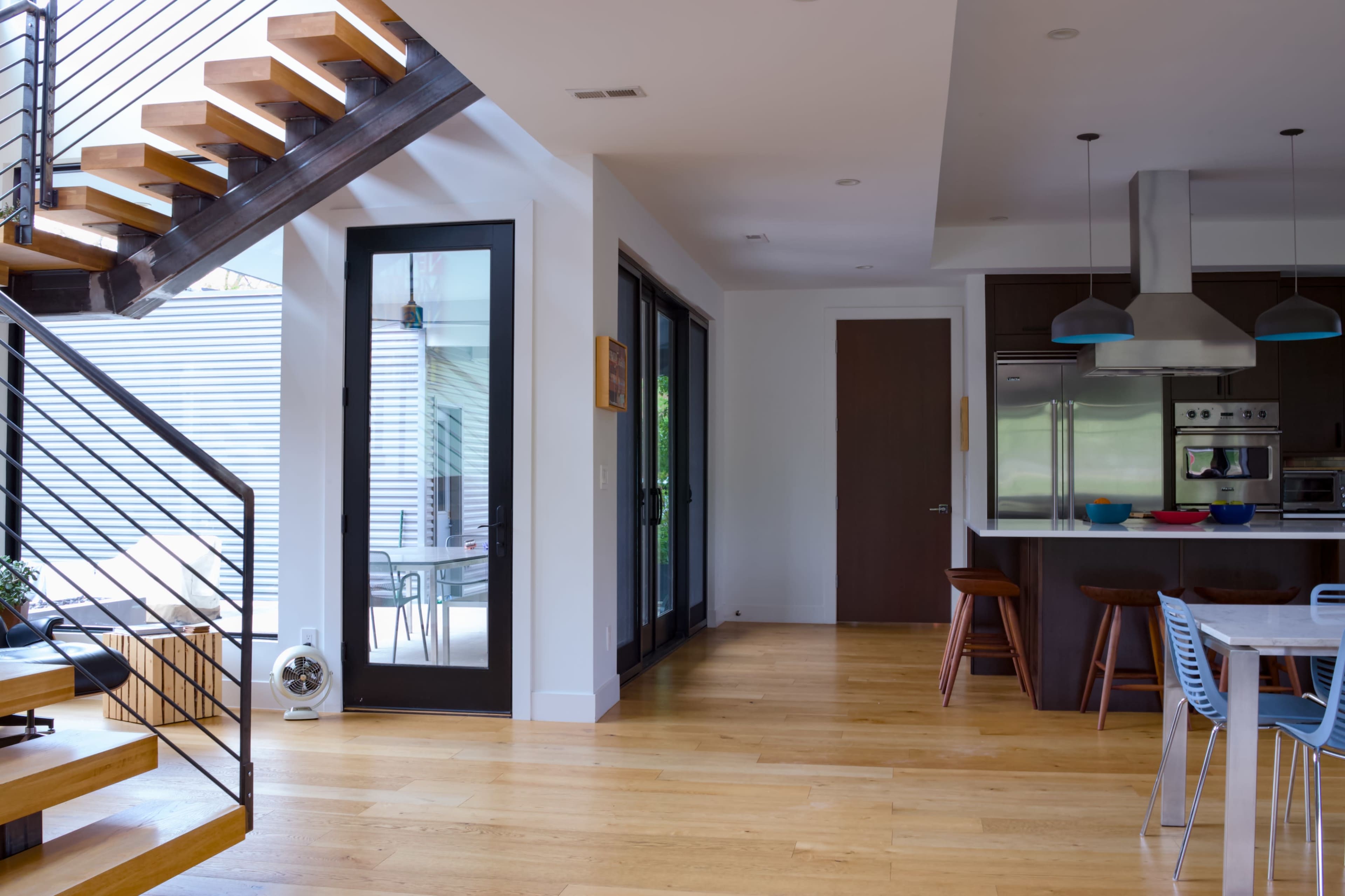A modern, open-concept interior features a staircase, a kitchen with bar stools, and a clear view of an outdoor dining area through large glass doors.