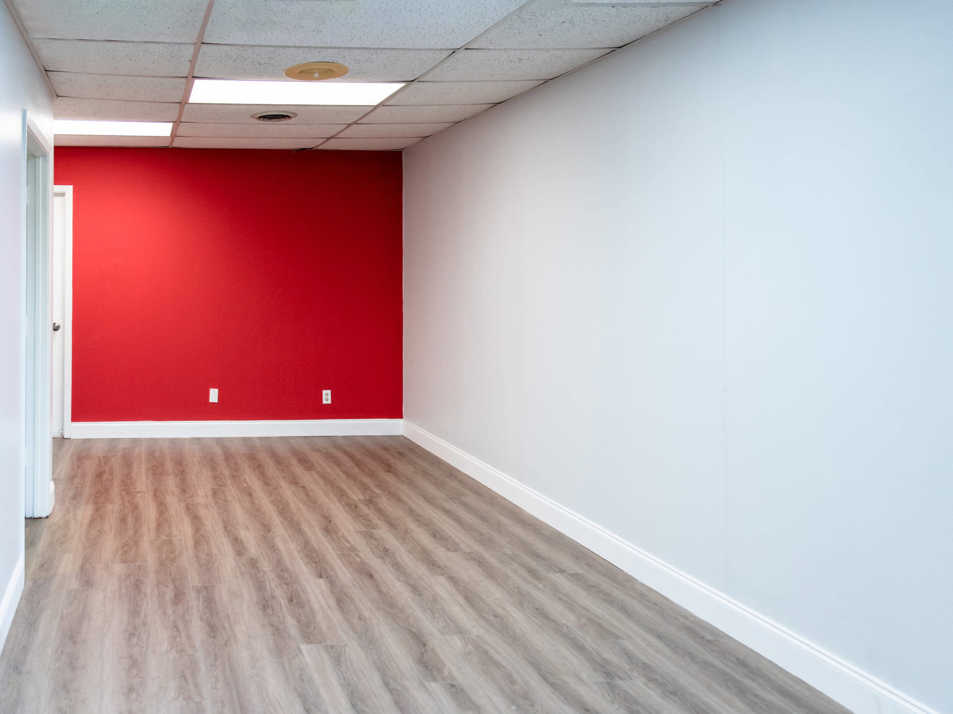 The image shows an empty room with a red accent wall and light-colored flooring.