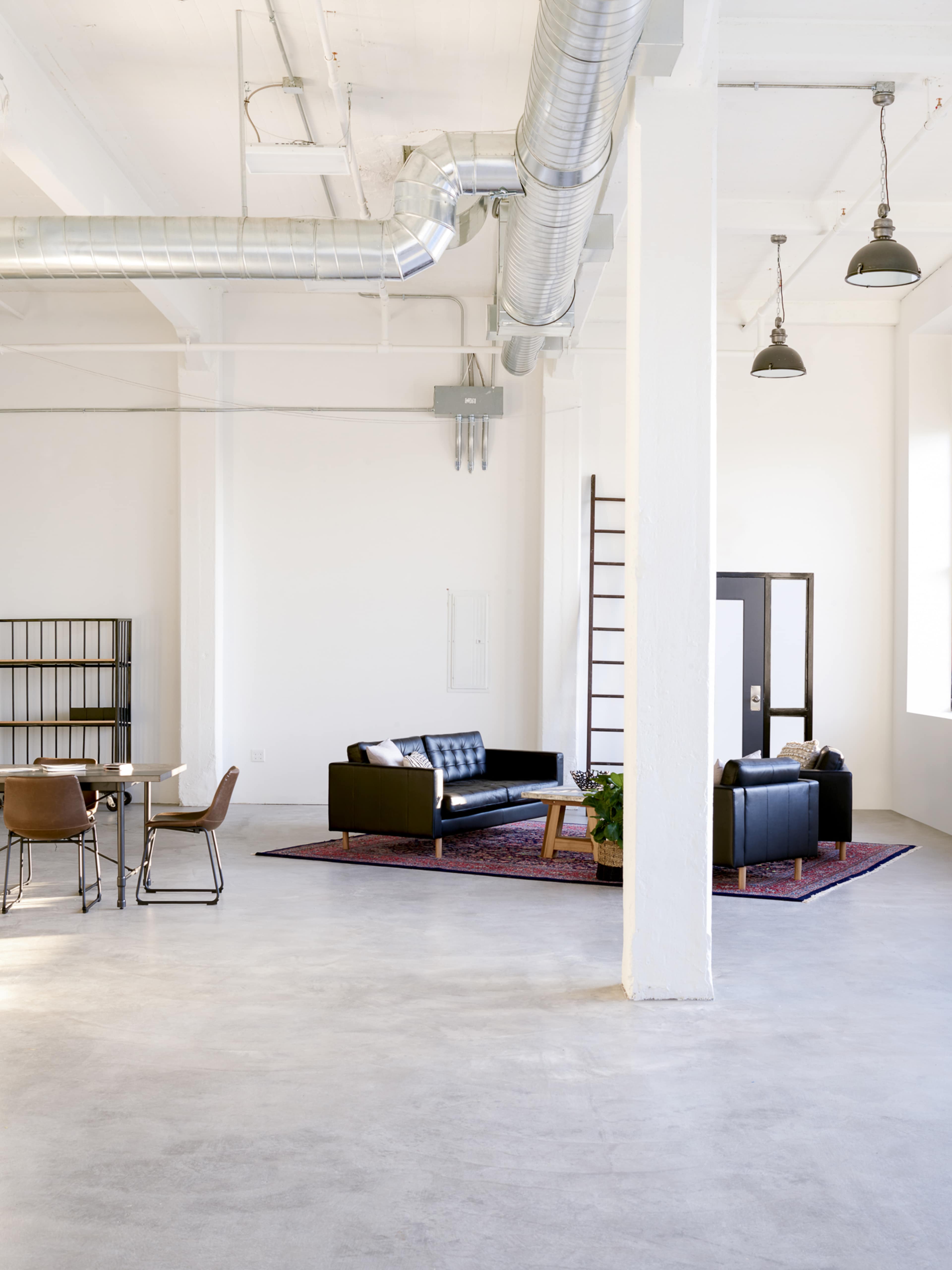 A spacious, modern room with a black sofa, a dining table, and industrial-style elements.