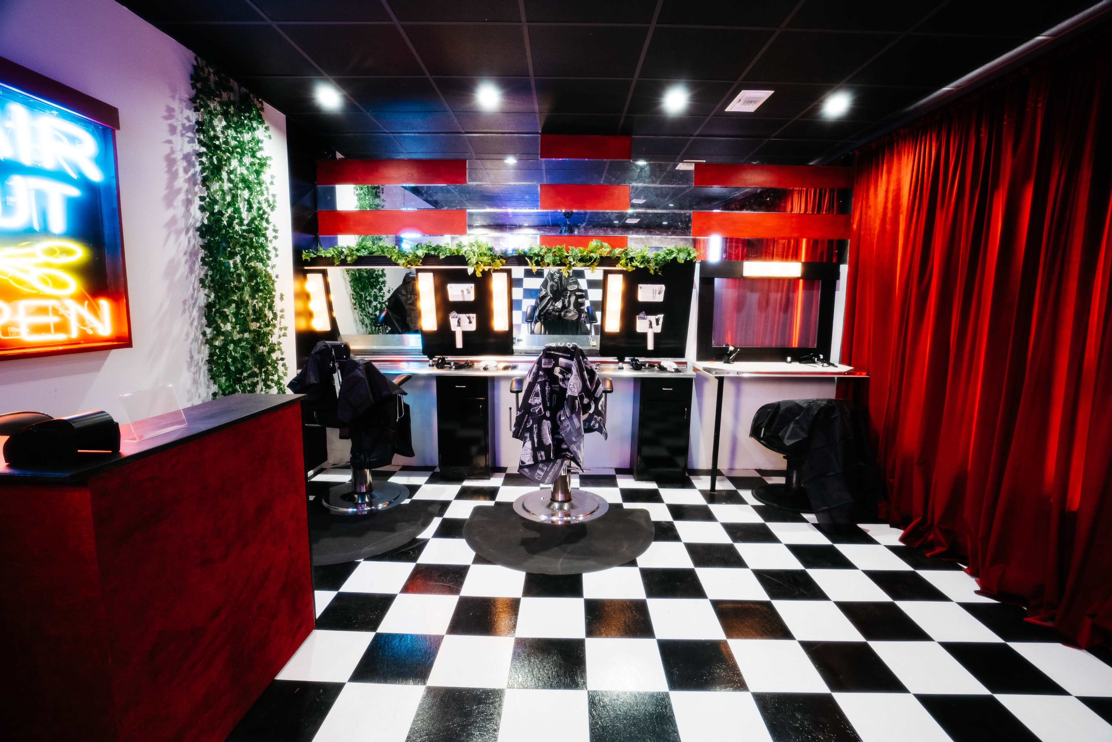 A modern hair salon with black and white checkered flooring, red curtains, and illuminated mirrors.