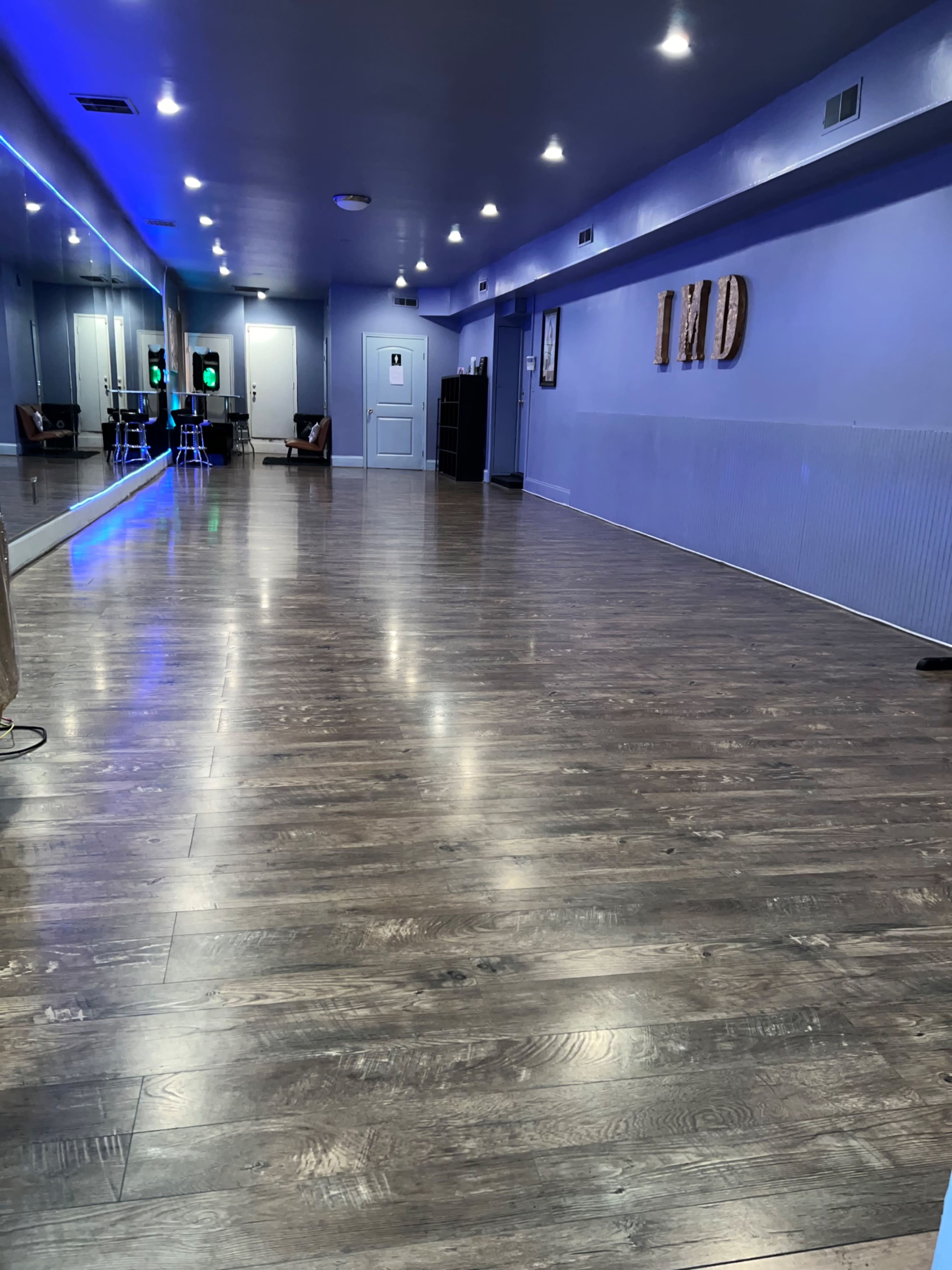 An empty dance studio with wooden flooring, mirrors along one wall, and ambient lighting.