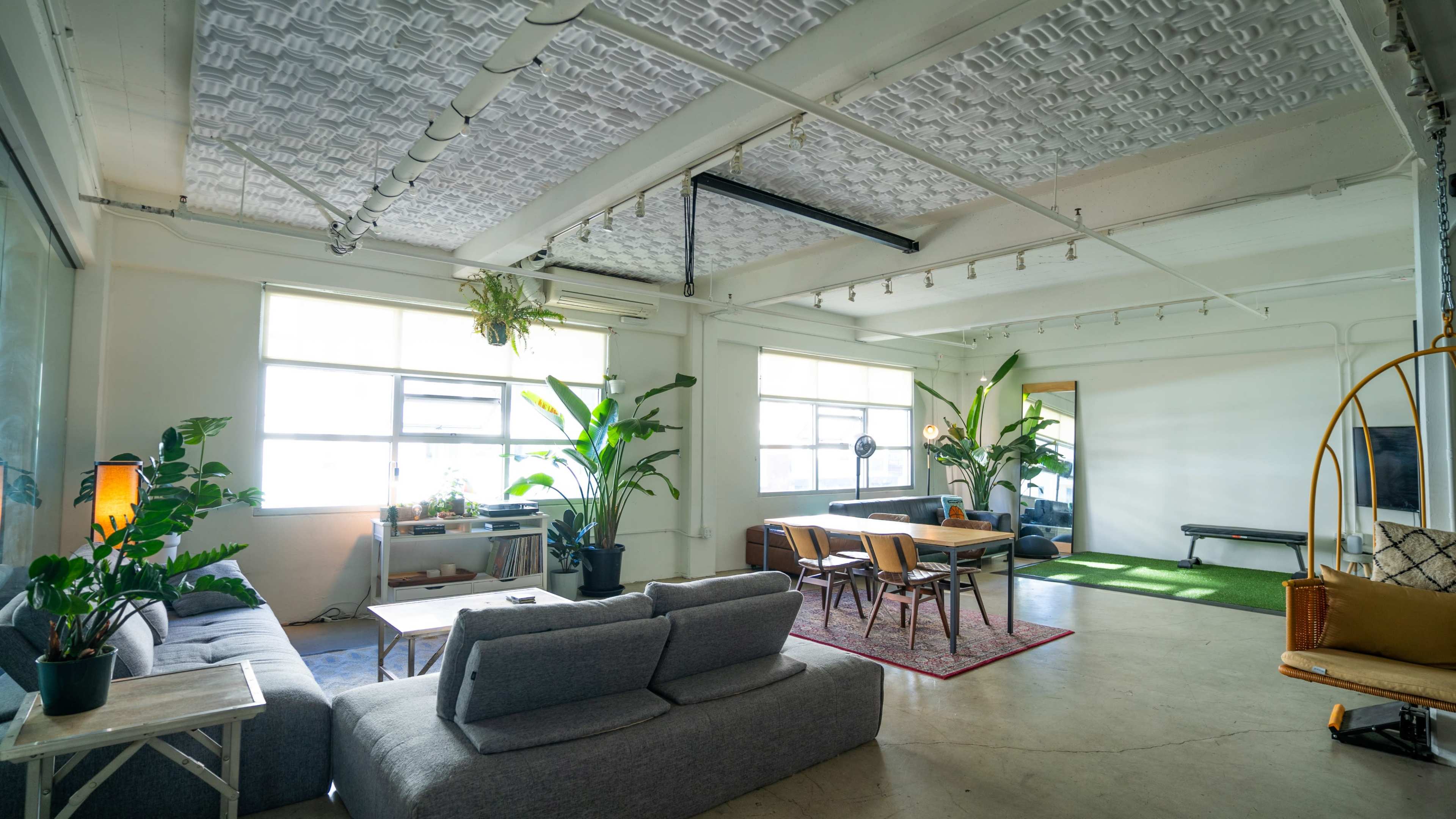 A spacious, modern living area featuring a seating area with gray sofas, a dining table with chairs, and large windows allowing natural light.