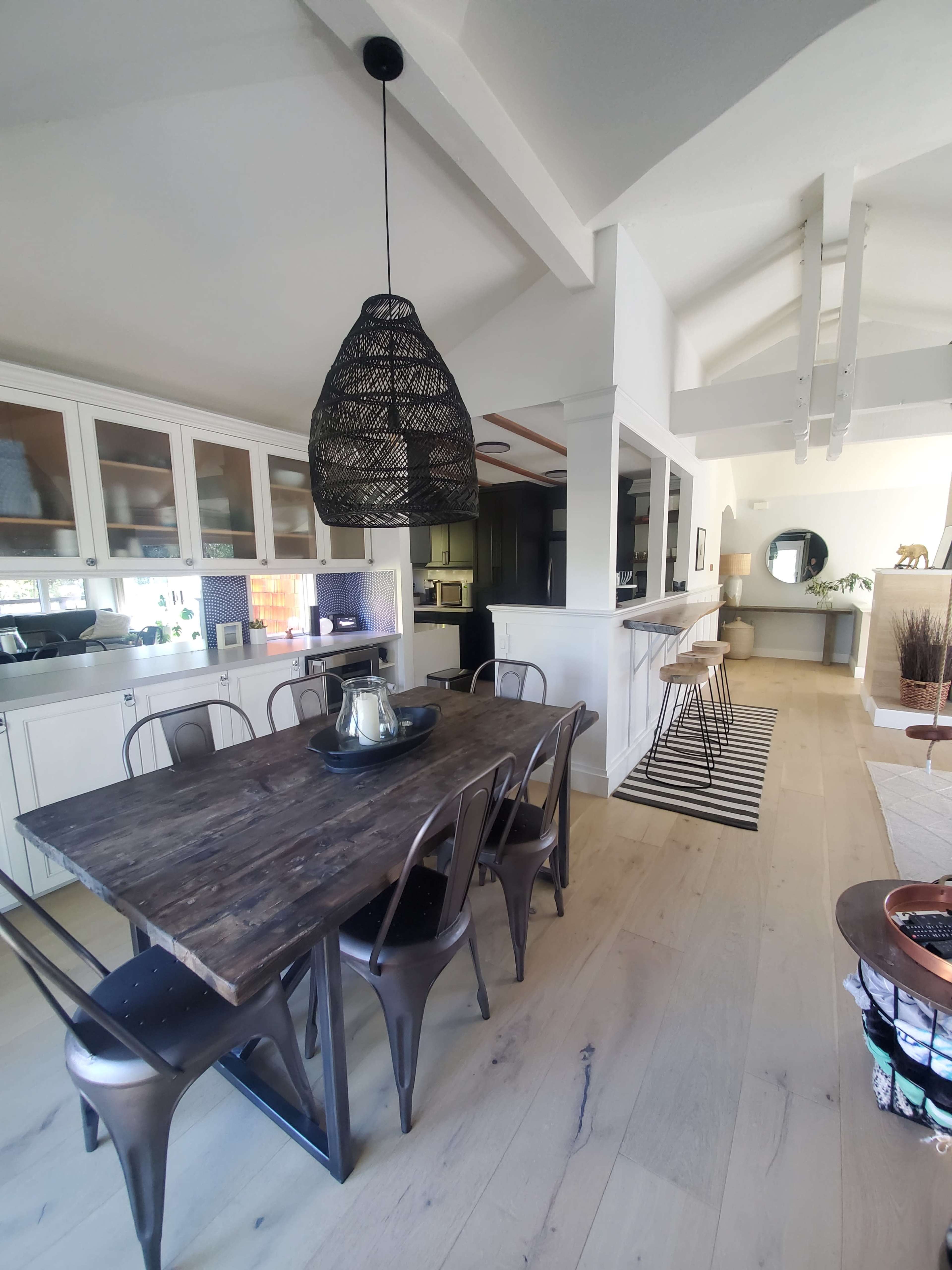 The image shows a modern kitchen and dining area with a wooden table surrounded by metal chairs, and a large pendant light hanging above.