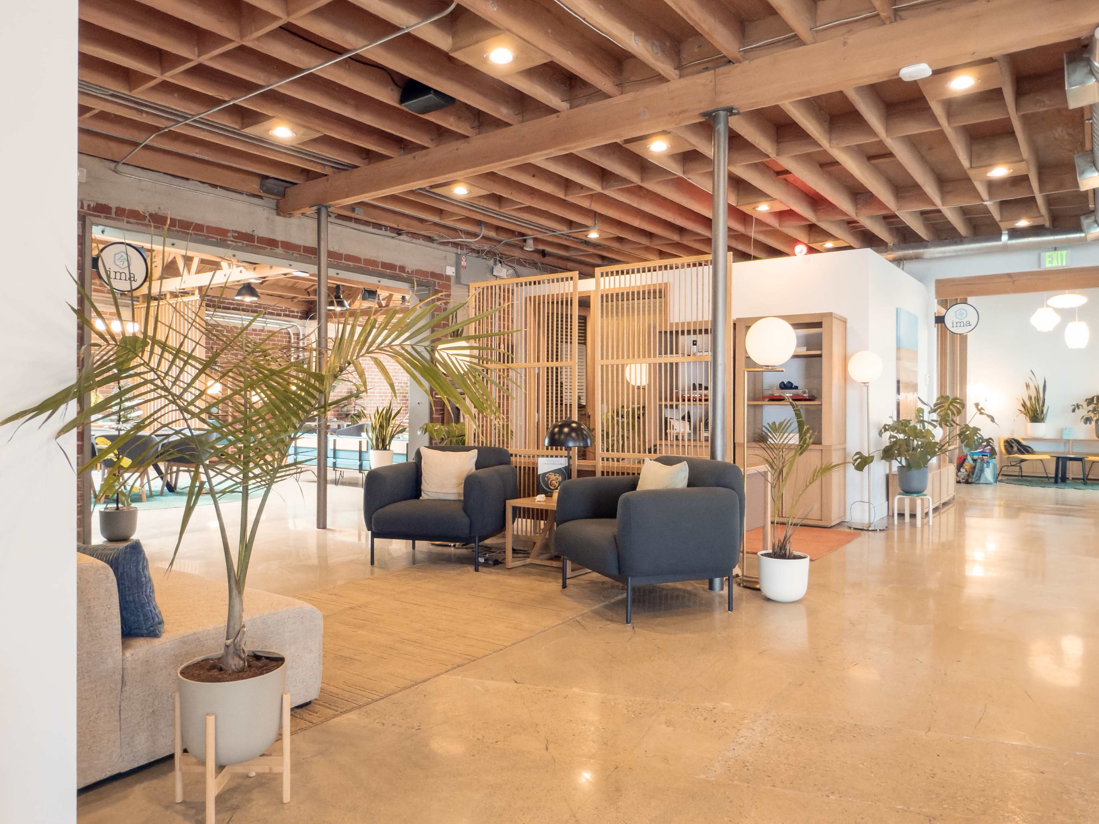 The image shows a modern, open-concept interior space featuring comfortable seating arrangements, decorative plants, and partitioned sections for various activities.