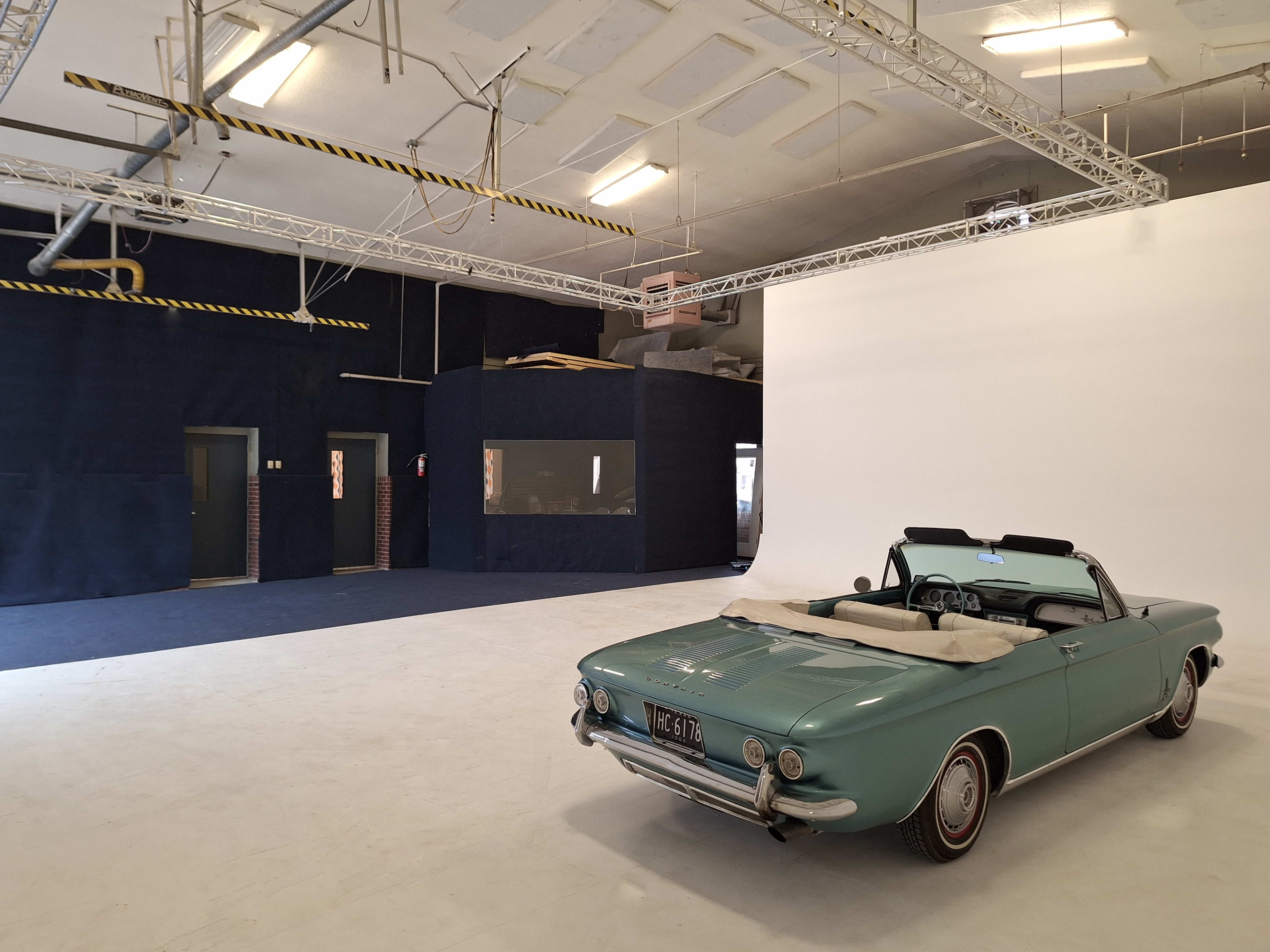 A vintage convertible car parked in a spacious, well-lit studio with white and dark blue backgrounds.