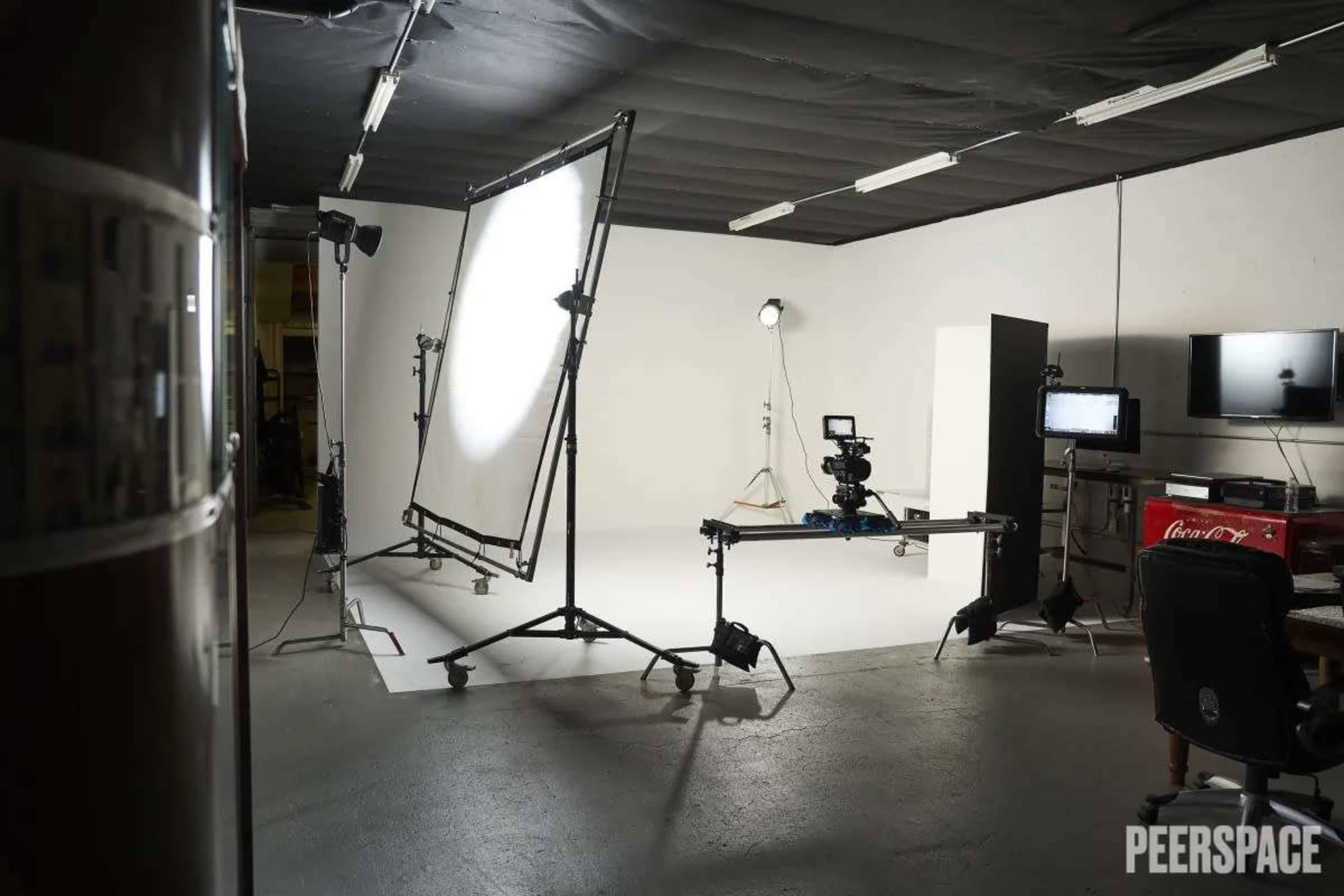 The image shows a studio setup with lighting equipment, a camera on a tripod, and a gray backdrop.