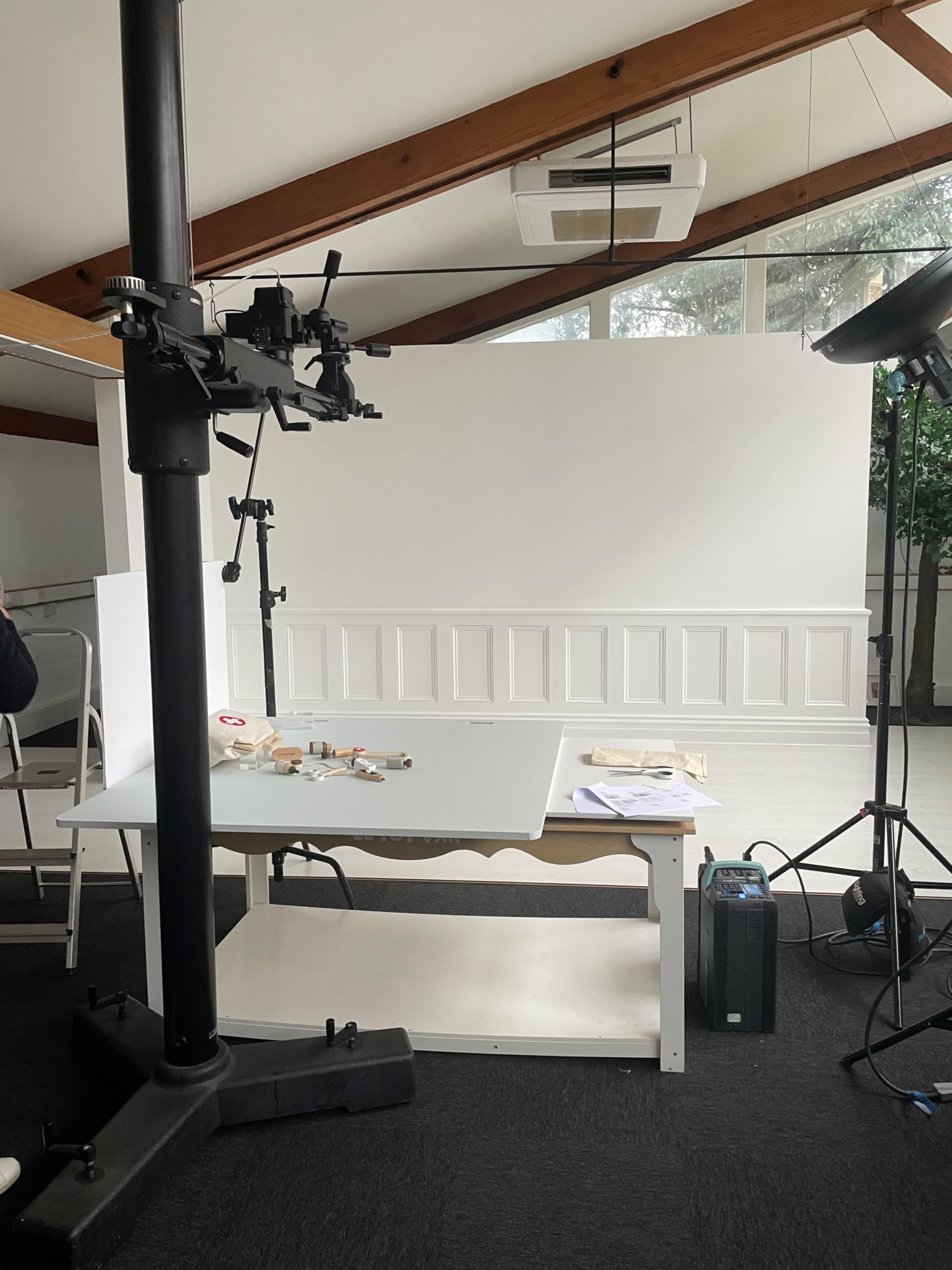 A photography setup in a bright room, featuring a large white backdrop, a table with various materials, and lighting equipment.