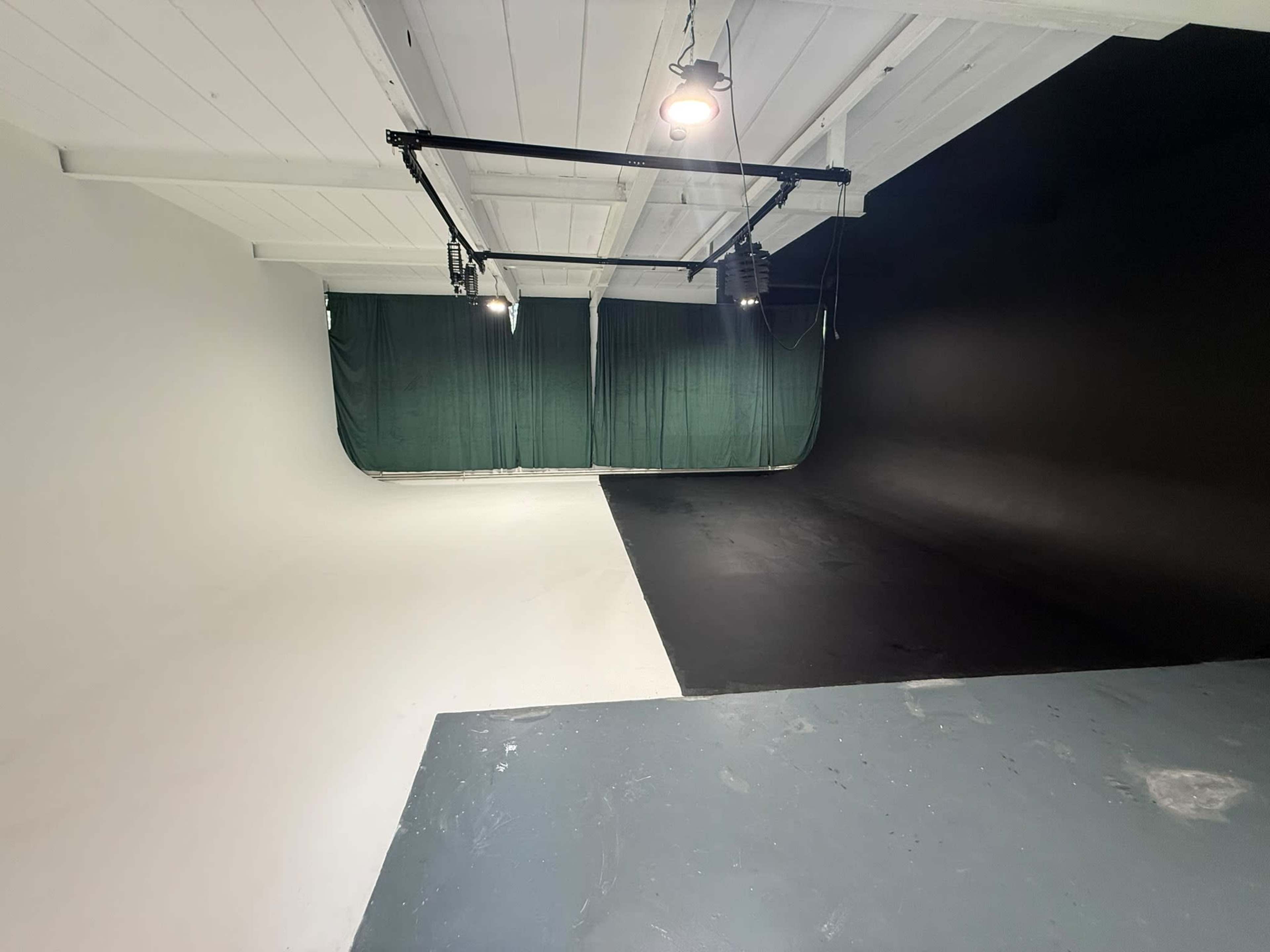 The image shows a studio space divided into two sections, one with a white backdrop and the other with a black backdrop, featuring overhead lights.