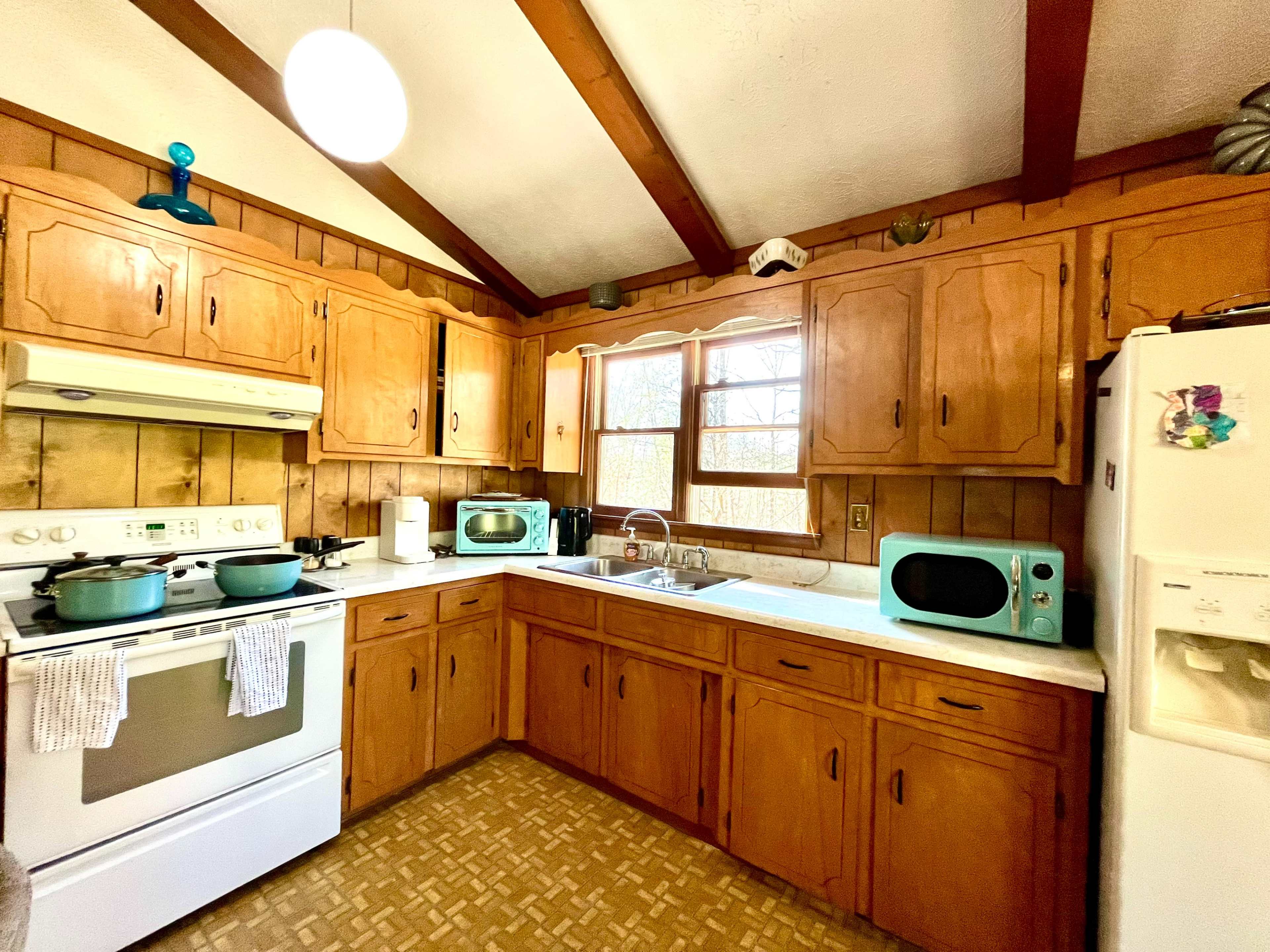 A wooden kitchen with a stove, microwave, and sink under a window with brown cabinets lining the walls.