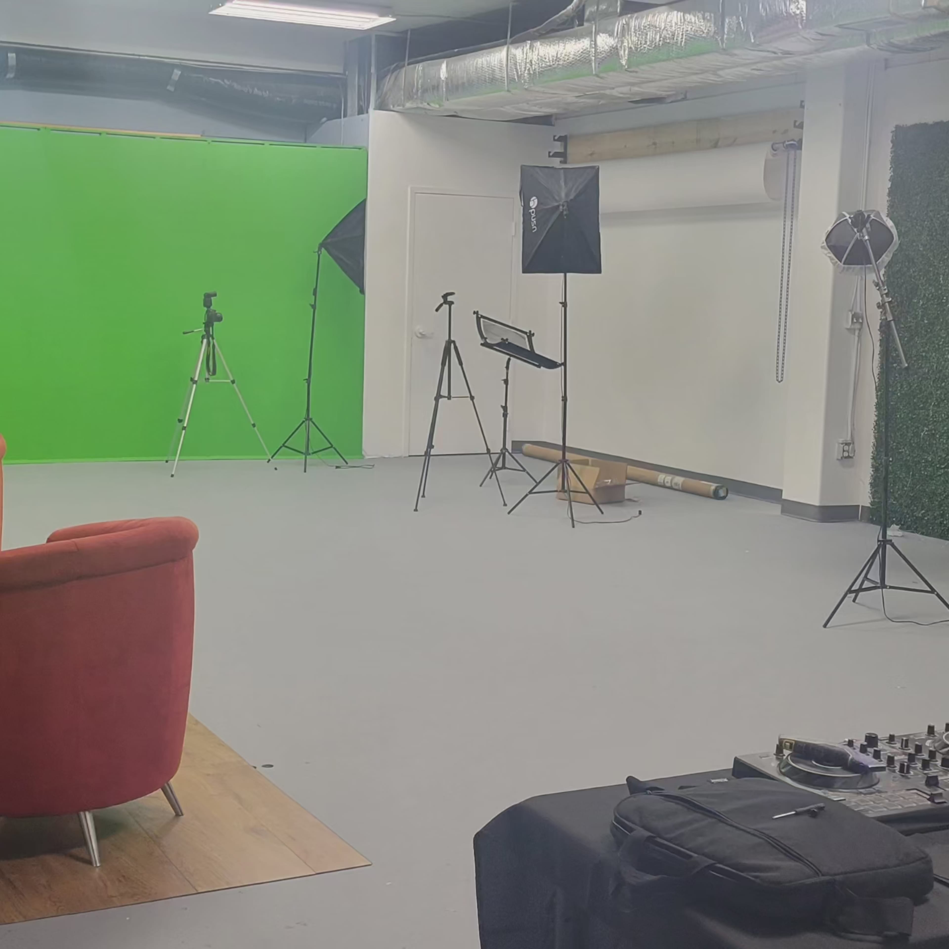 A studio setup with a green backdrop, various camera tripods, lighting equipment, and a sound mixer on a table.