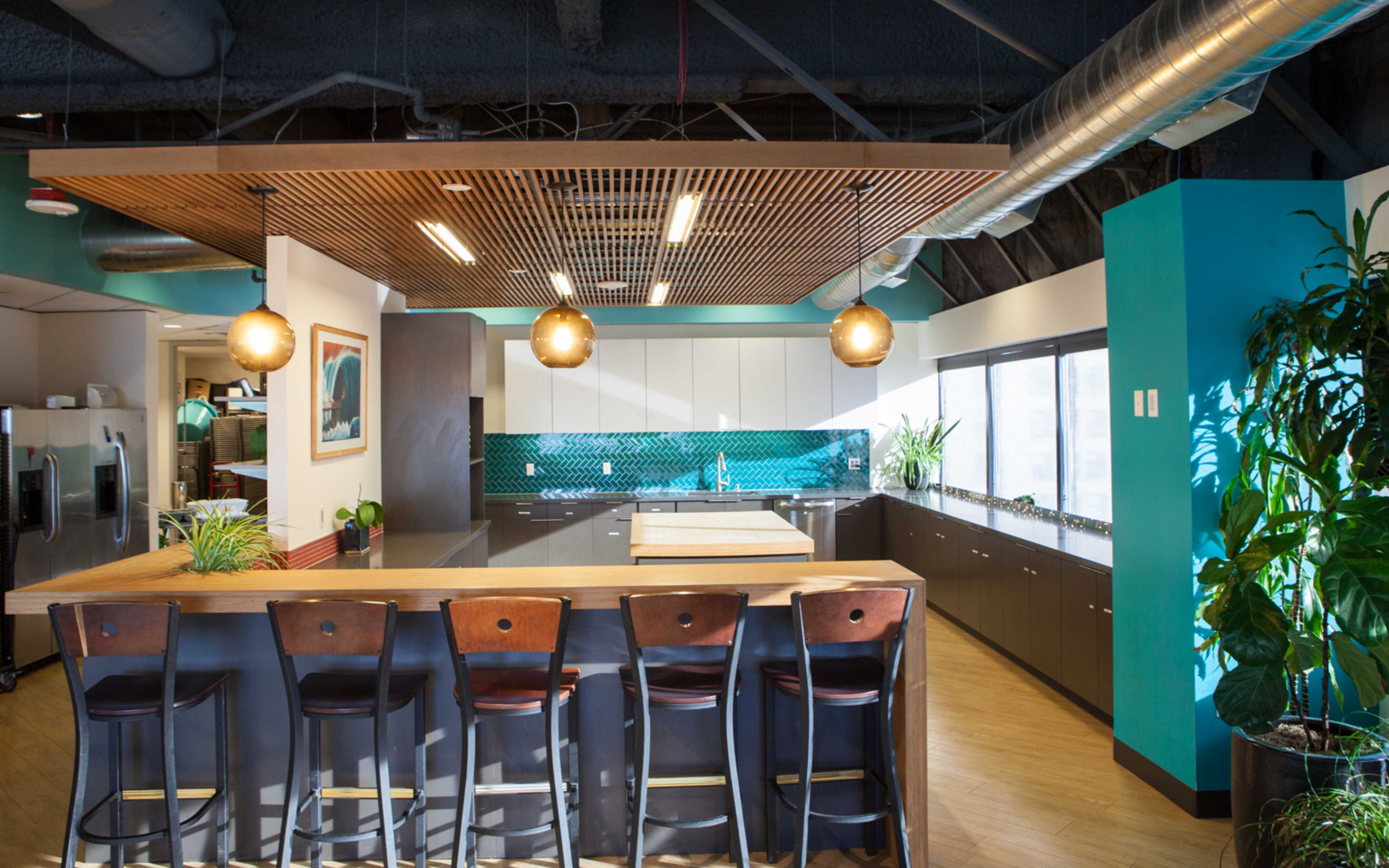 A modern kitchen with a central island, bar stools, and large windows allowing natural light to enter.