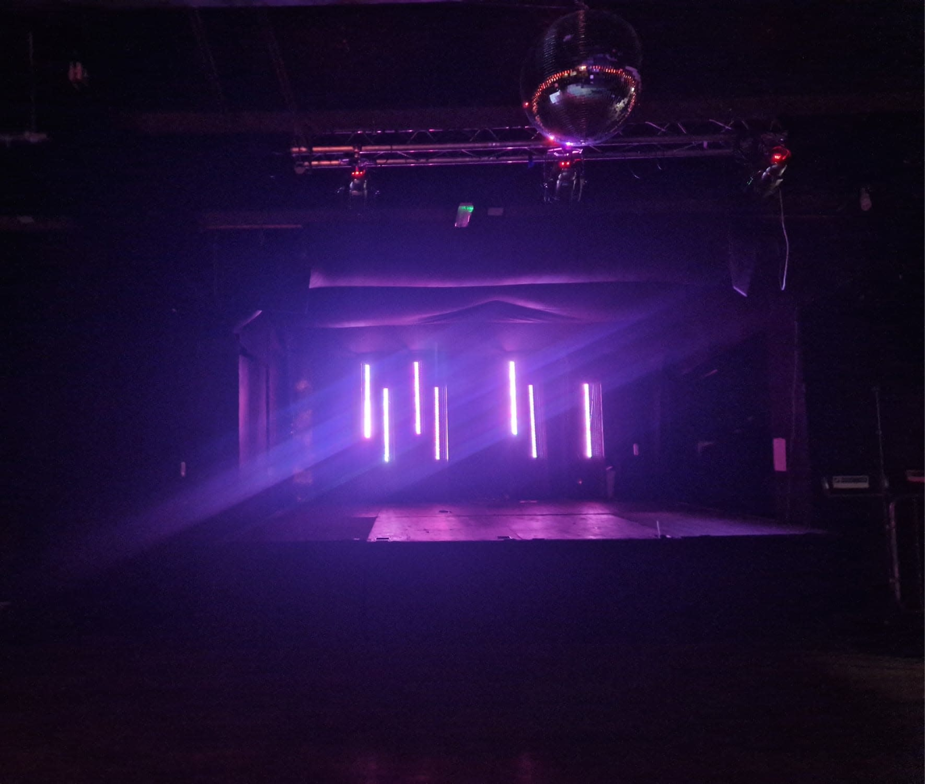 A dimly lit stage features vertical LED lights and a disco ball hanging above.