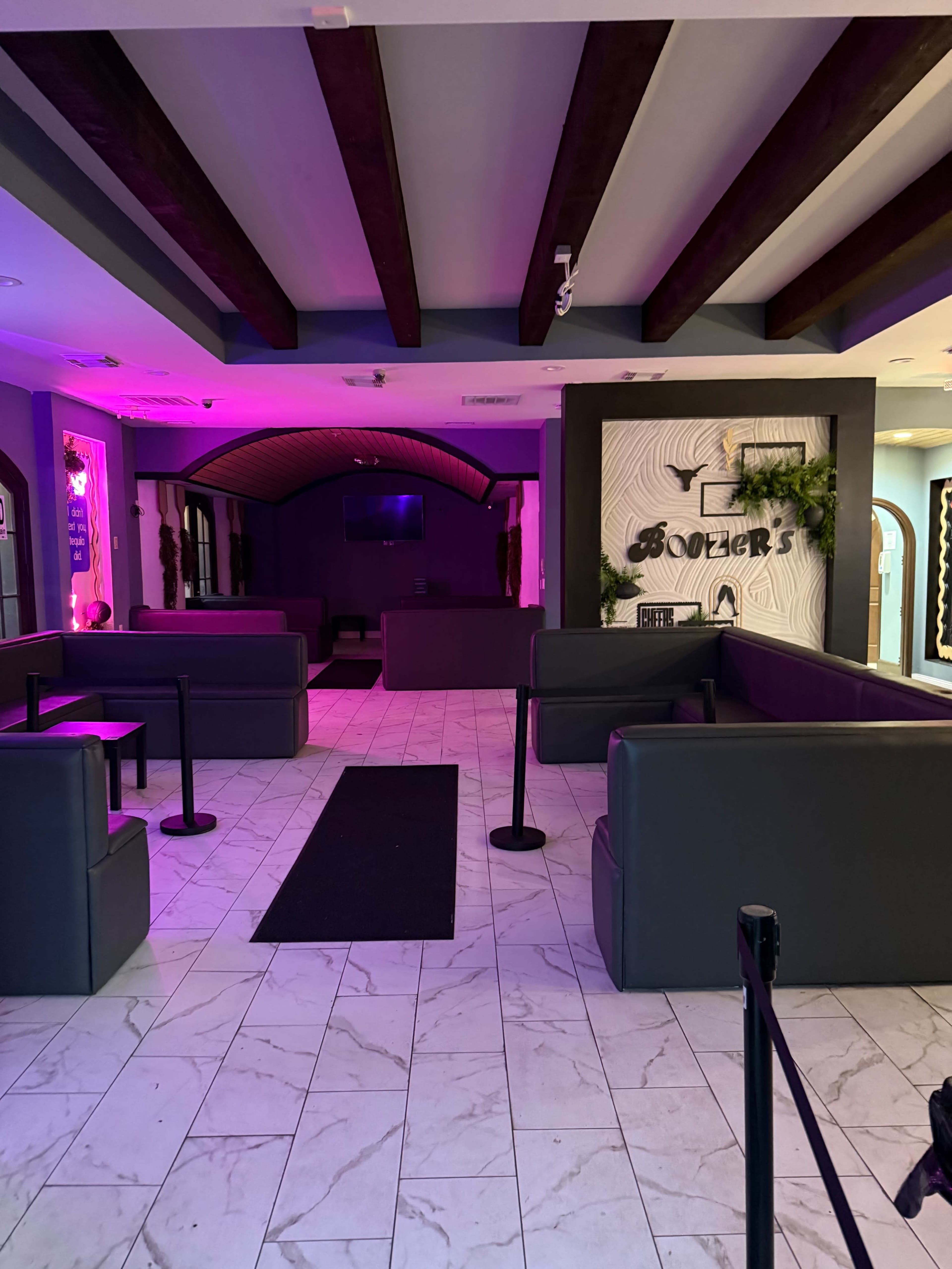 The image shows a partially lit lounge area with dark leather seating, a minimalist decor, and a television mounted on the wall in the background.