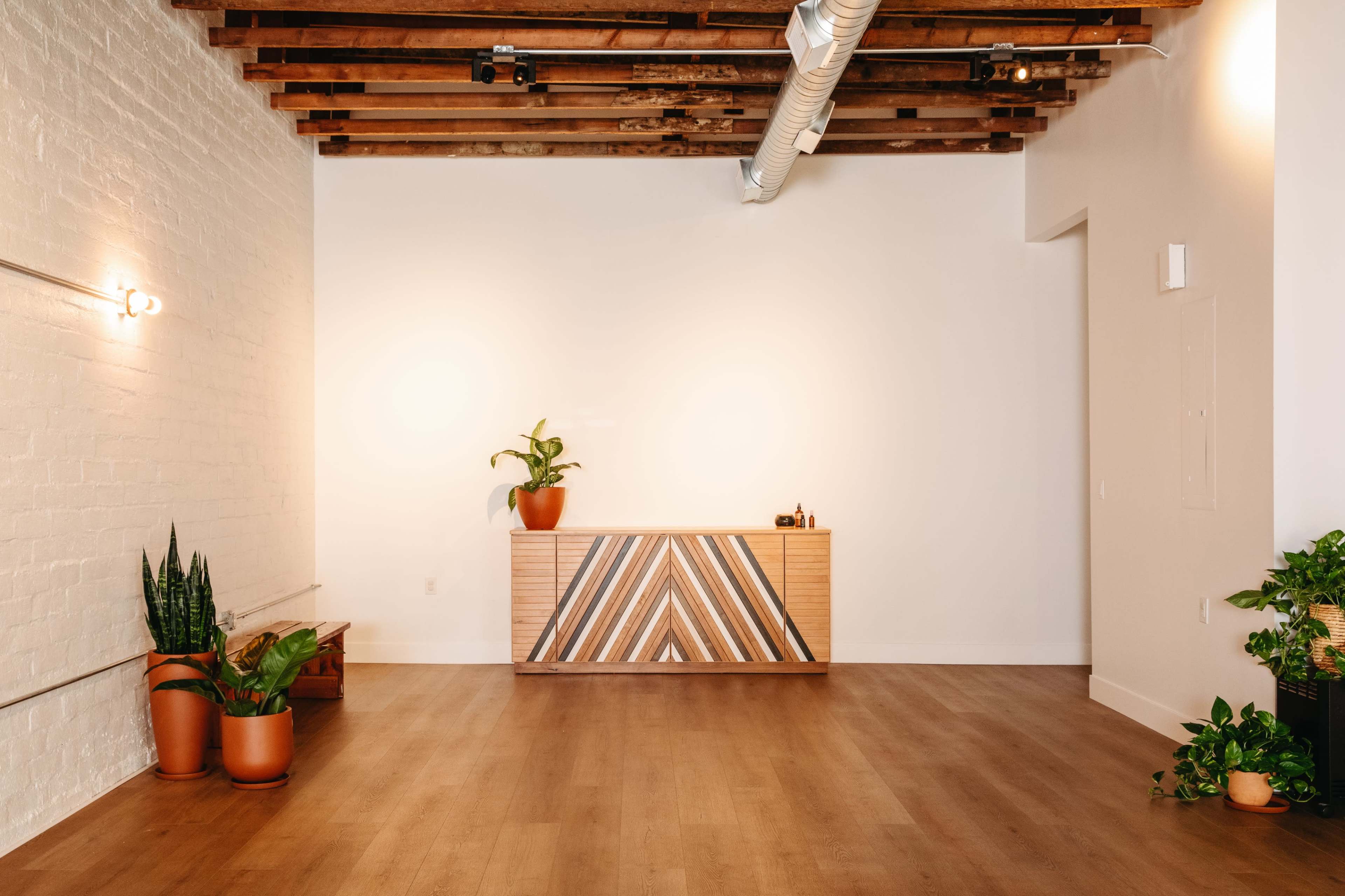 A spacious and minimalist reception area featuring a wooden desk and several potted plants against a white wall.