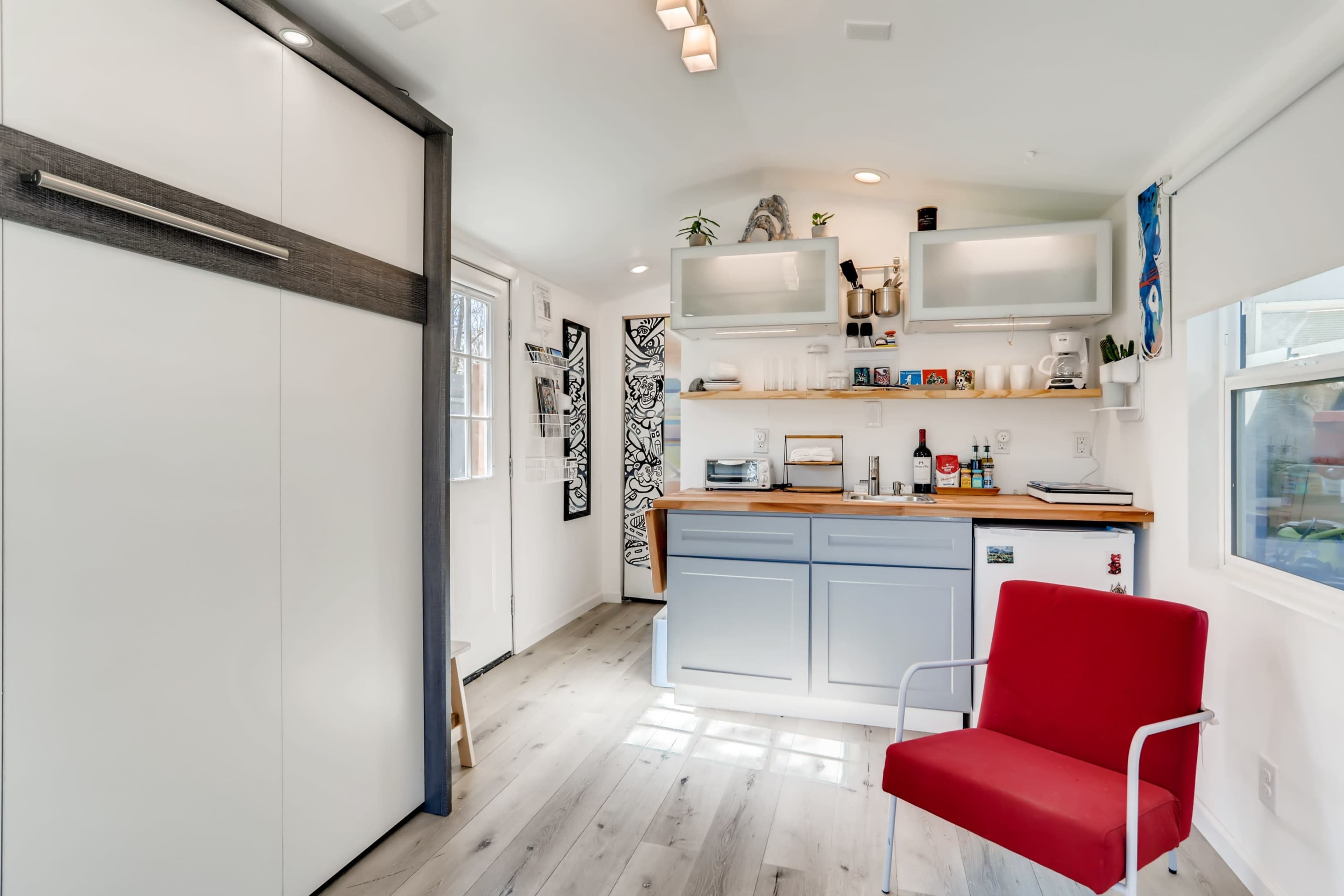 A compact, modern kitchen space featuring a red chair, a countertop with appliances, and white cabinetry.