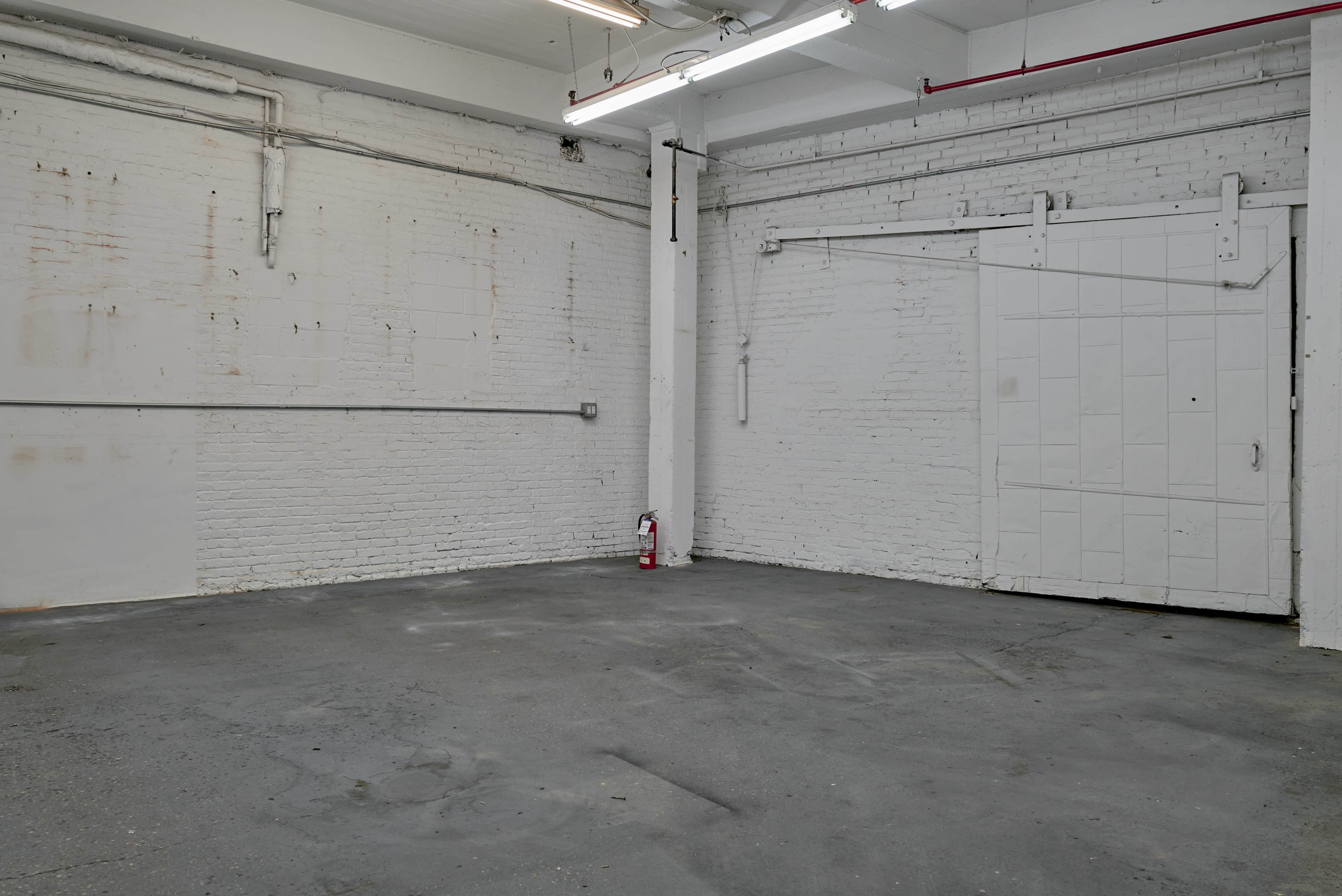 The image shows an empty industrial space with white brick walls, concrete flooring, and a closed door on one side.