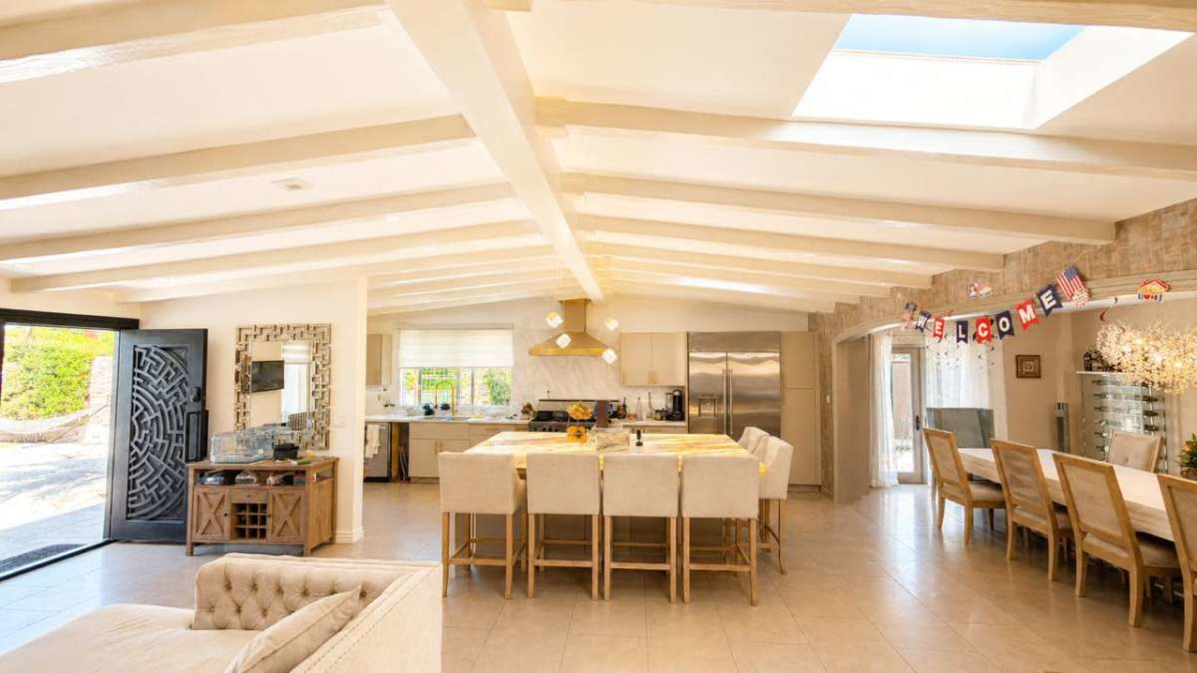 The image depicts a spacious and well-lit open-concept living and dining area featuring a large kitchen island with bar seating.