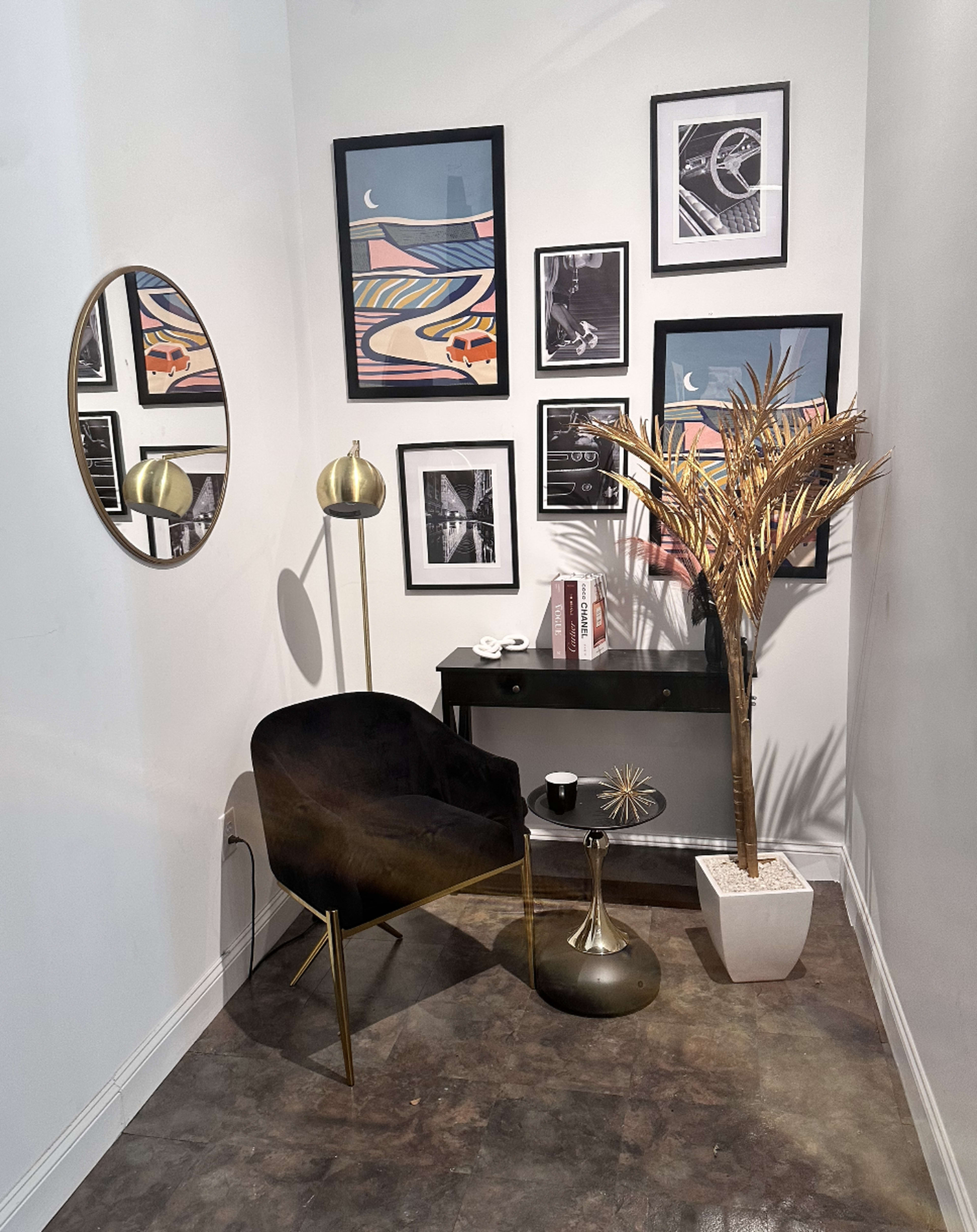 The image shows a cozy corner of a room featuring a black chair, a small side table, decorative wall art, and a potted plant.