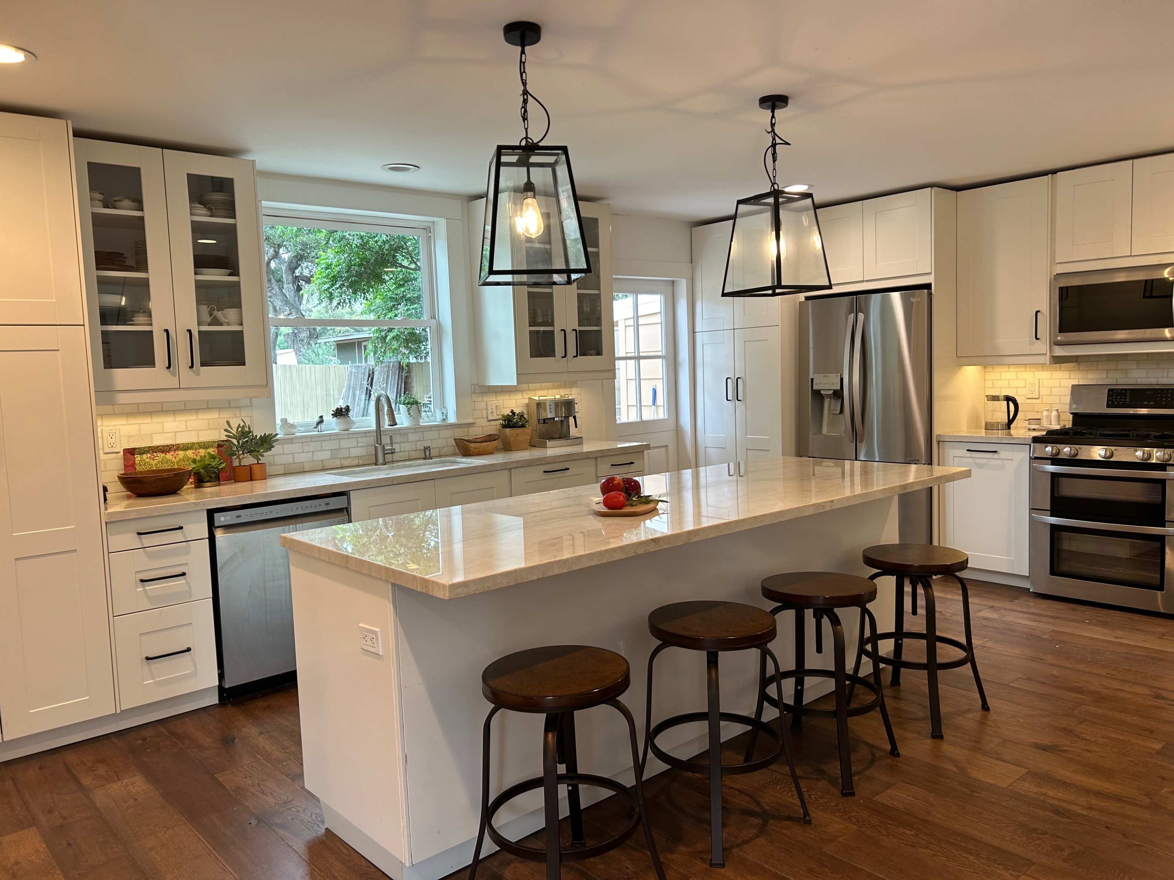 A modern kitchen with white cabinetry, stainless steel appliances, and a central island with four bar stools.