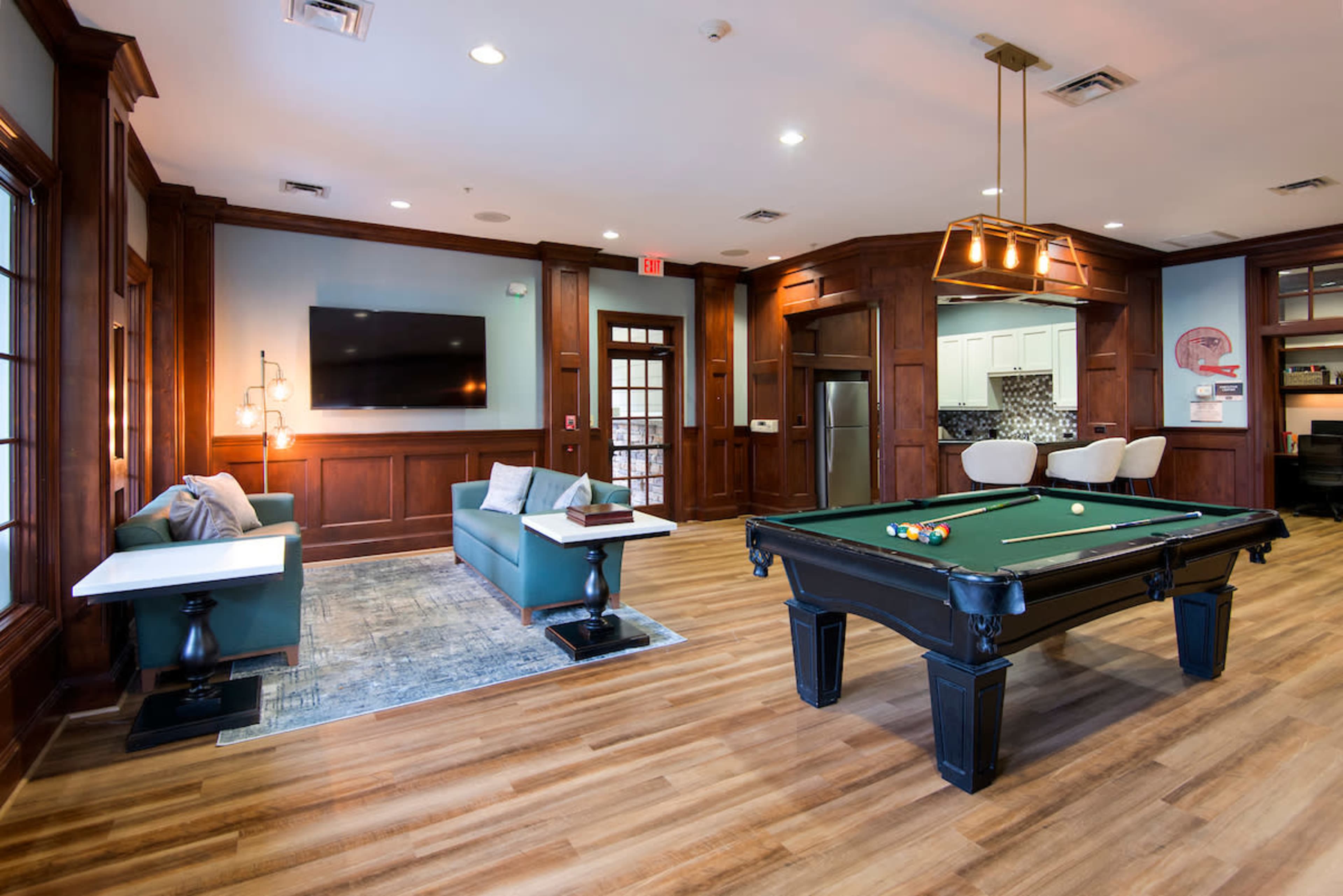 A modern lounge area featuring a pool table, a large television on the wall, and seating arrangements with wooden paneling.