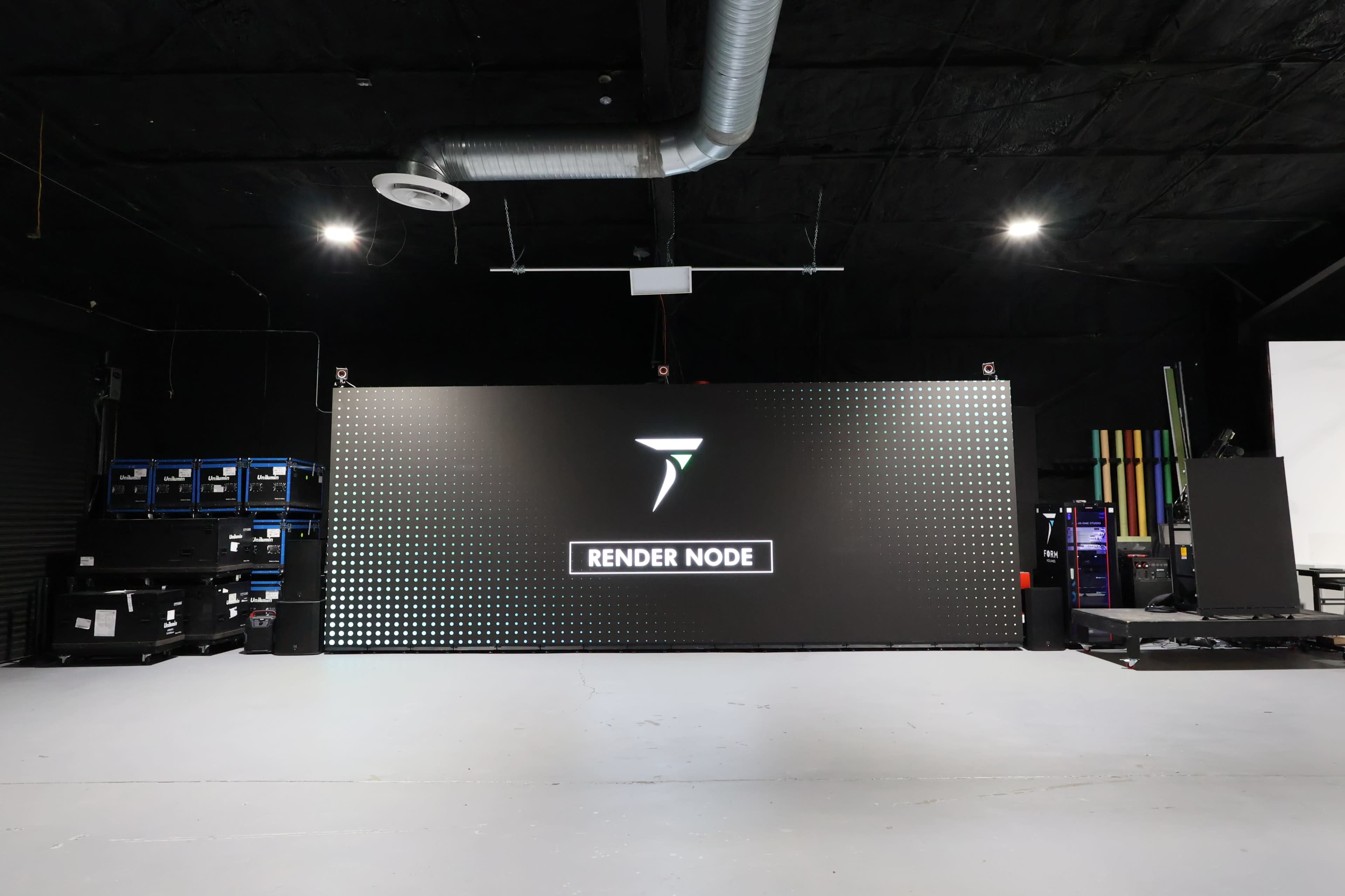 The image shows a large digital display screen with the text "RENDER NODE" on it, set in a dark room with various equipment in the background.