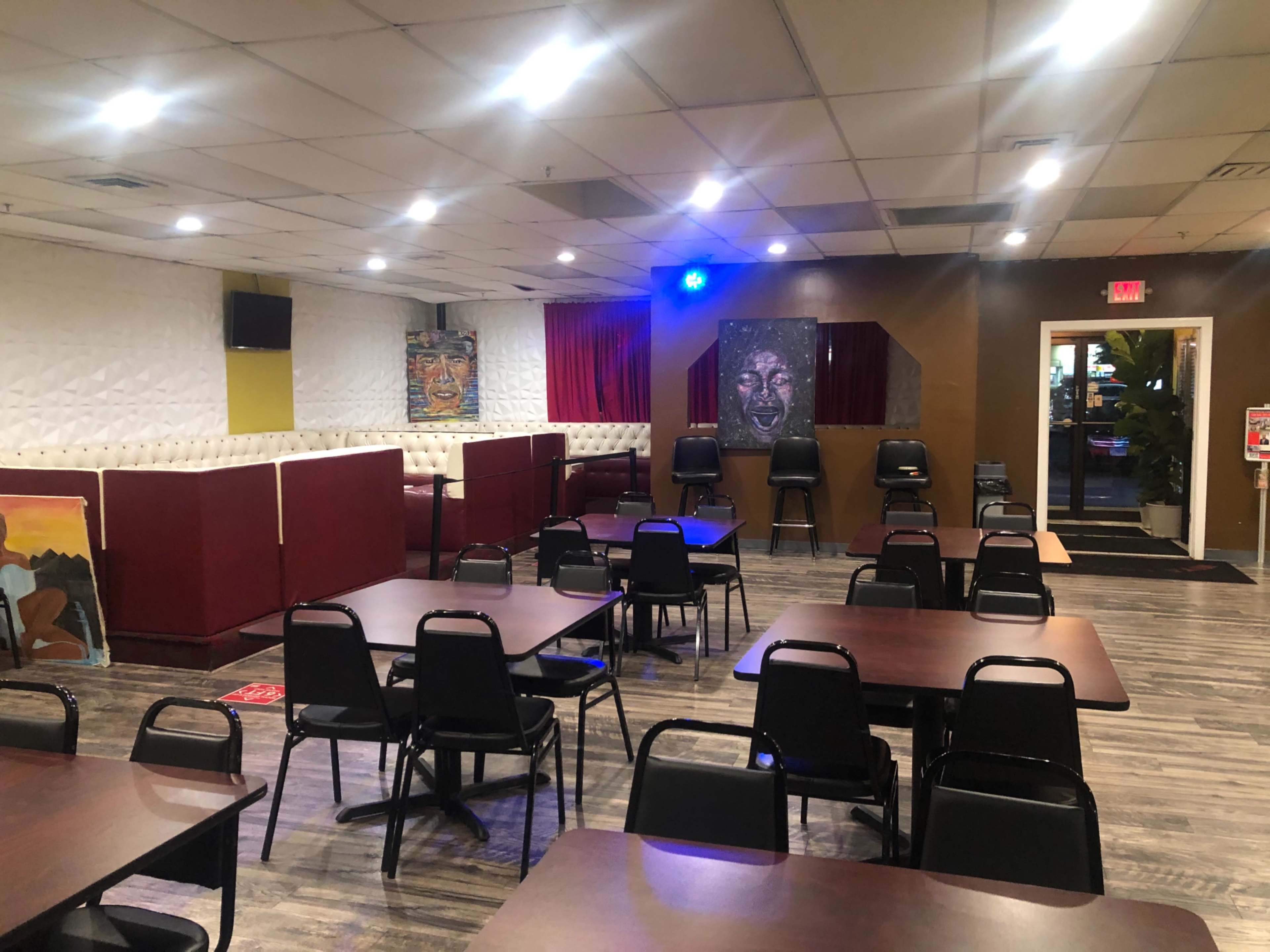 An empty dining area with tables and chairs, featuring a booth along one wall and artwork displayed on the opposite wall.