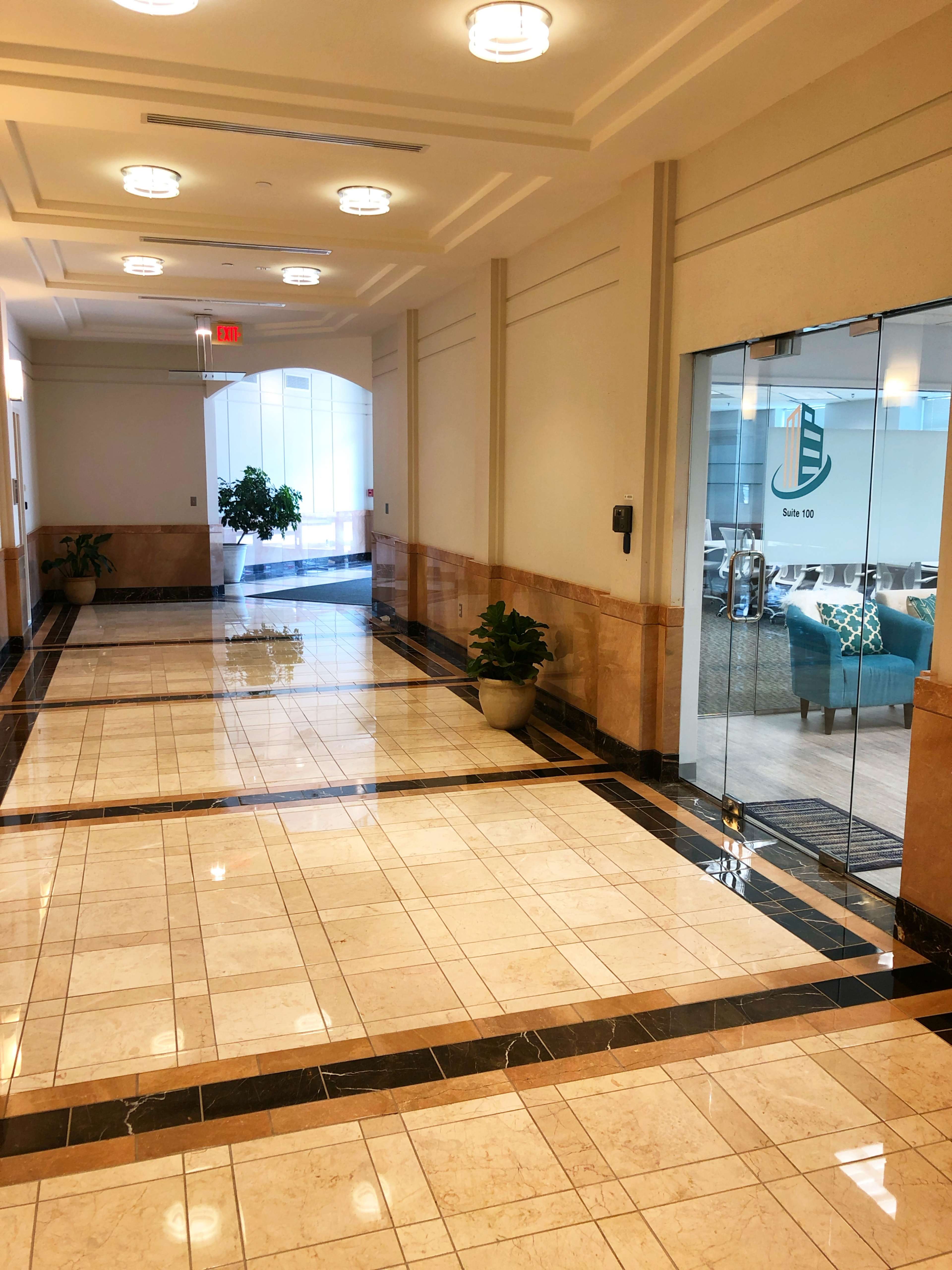 A well-lit hallway with polished tile floors leading to glass doors marked with a logo.