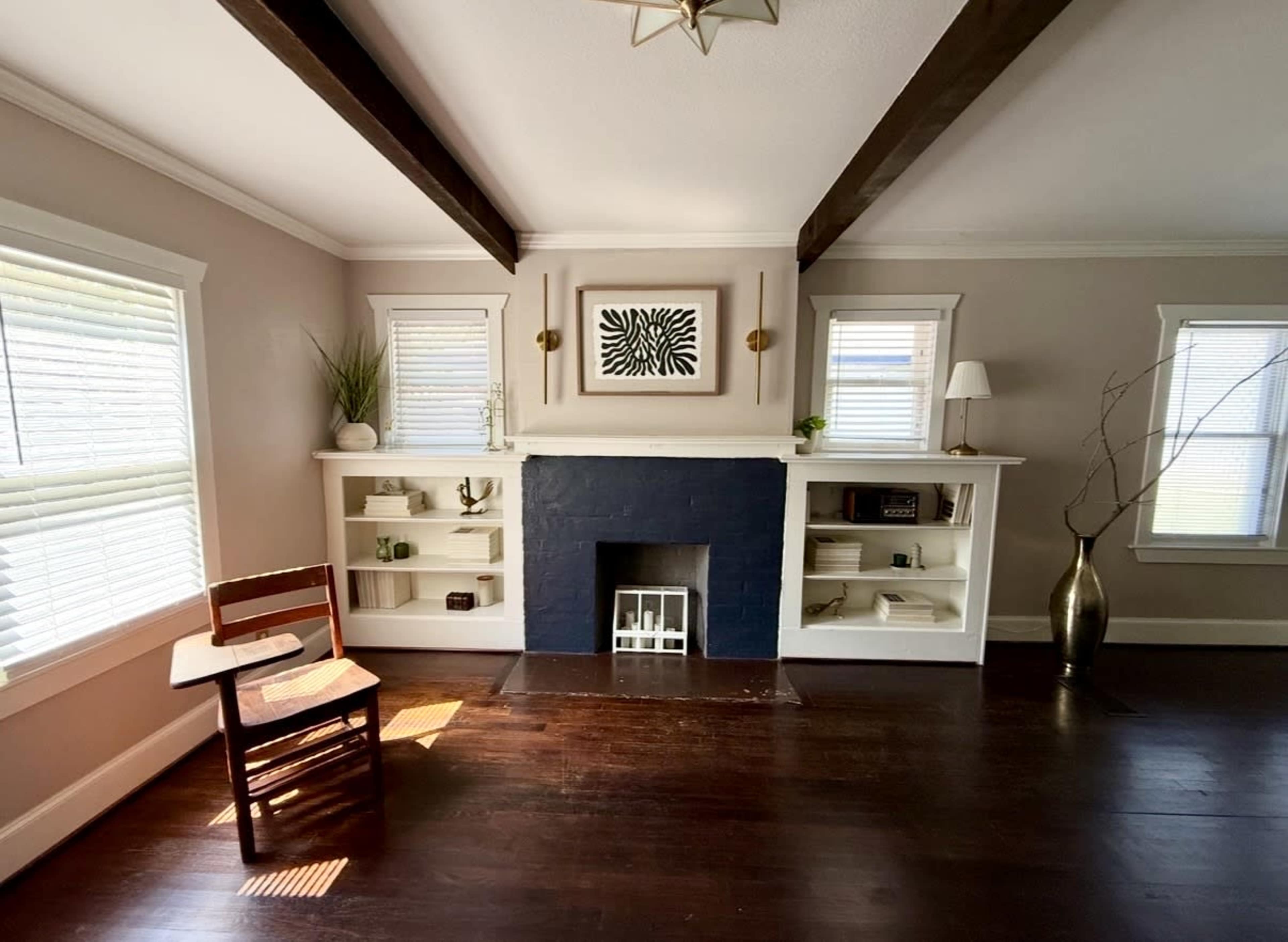 The image shows a living room with a black fireplace, built-in shelves on either side, a wooden chair on the floor, and natural light coming through the windows.