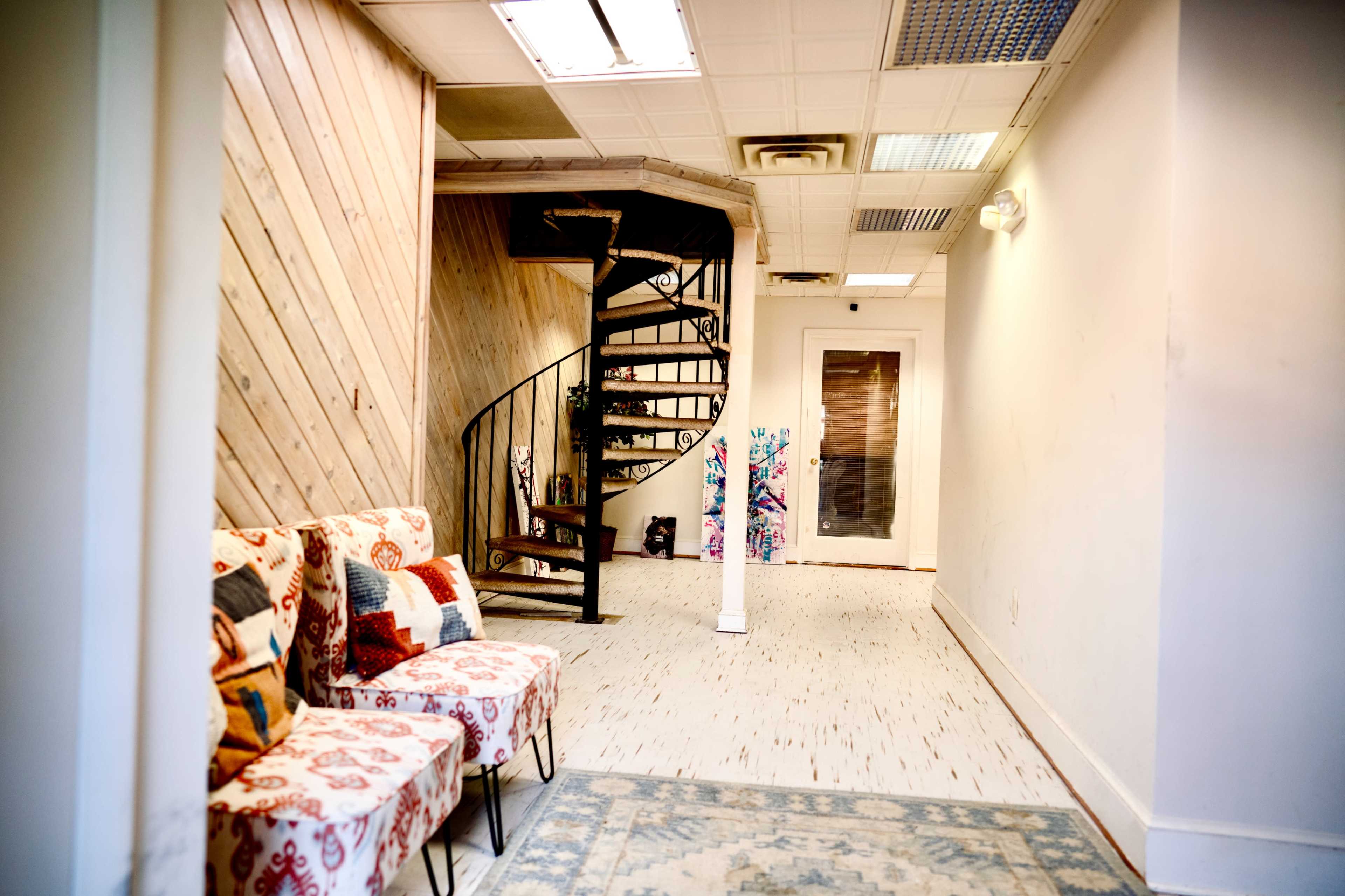 A hallway with two patterned chairs, a spiral staircase in the background, and a door covered with colorful artwork.