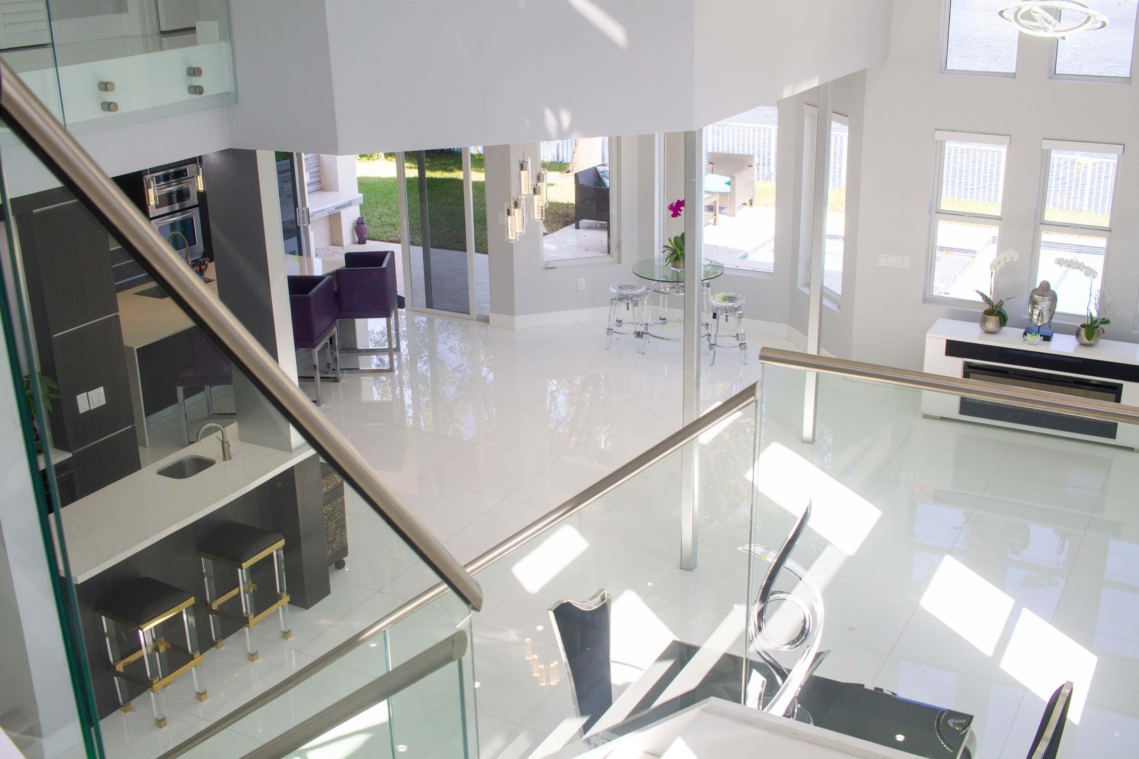 A modern, open-concept living space with a glass railing overlooking a bright, luminous area featuring sleek furniture and large windows.