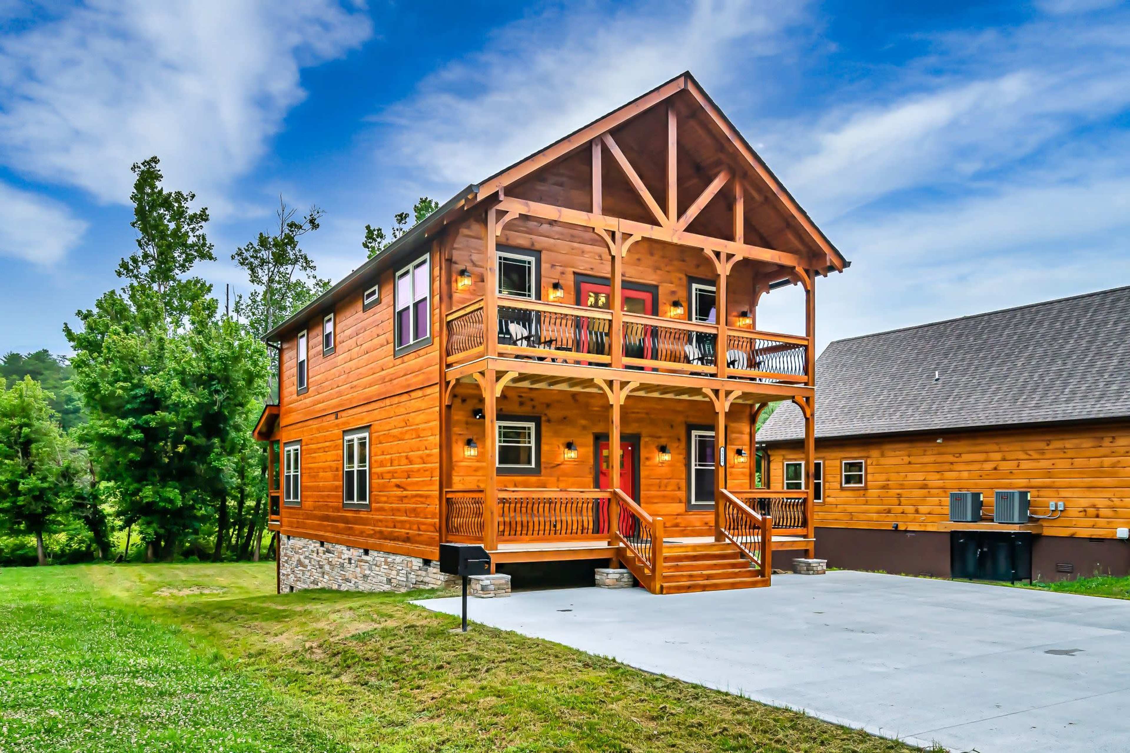 A two-story wooden house with a front porch, surrounded by a grassy area and trees in the background.