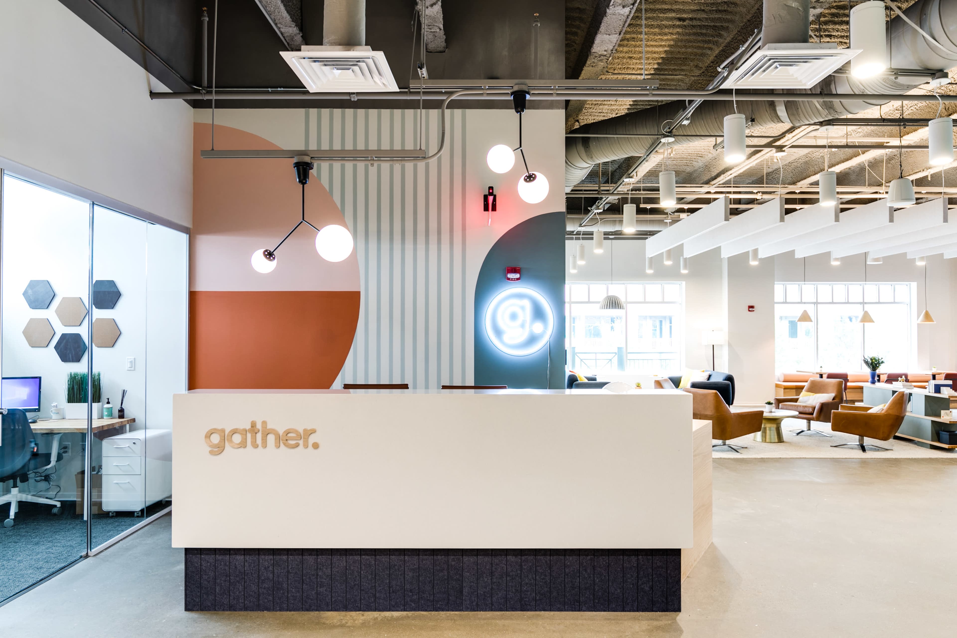The image shows a modern reception area with a clean white desk displaying the word "gather," surrounded by colorful wall accents and contemporary lighting fixtures.