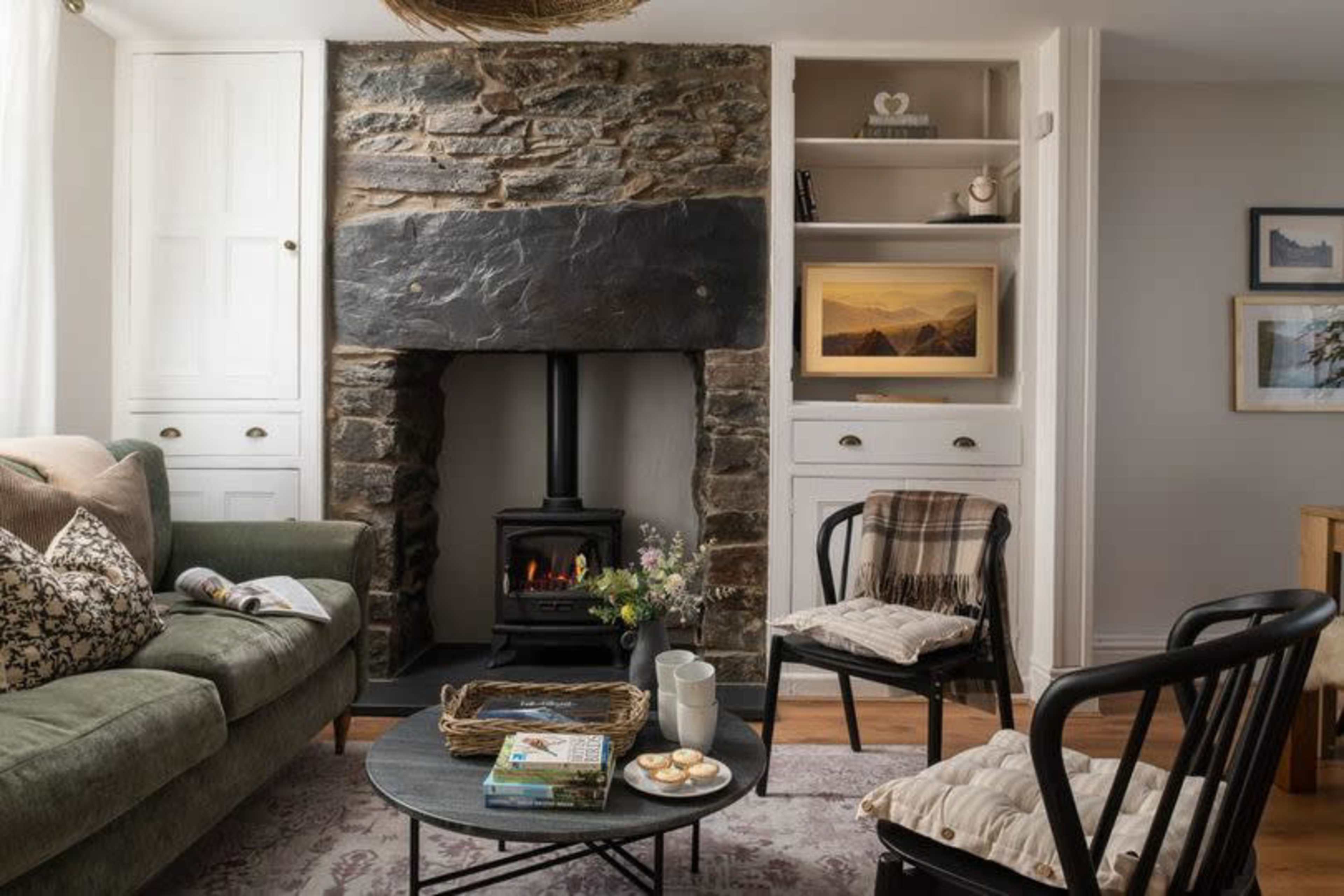 A cozy living room features a stone fireplace, a green sofa, and a round coffee table adorned with cookies and a magazine.