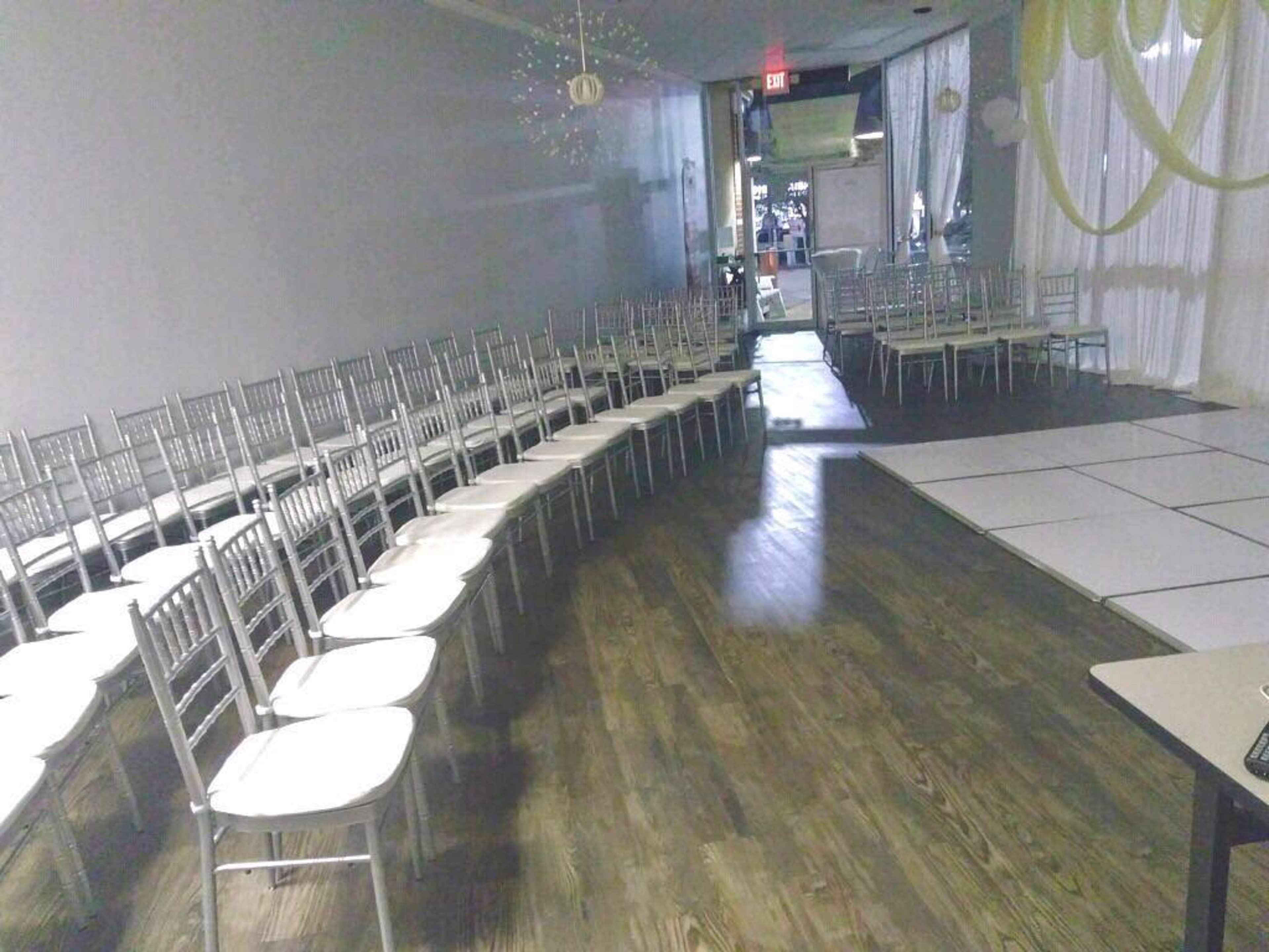The image shows a room set up for an event, featuring rows of silver chairs arranged in a curved formation alongside a white dance floor.