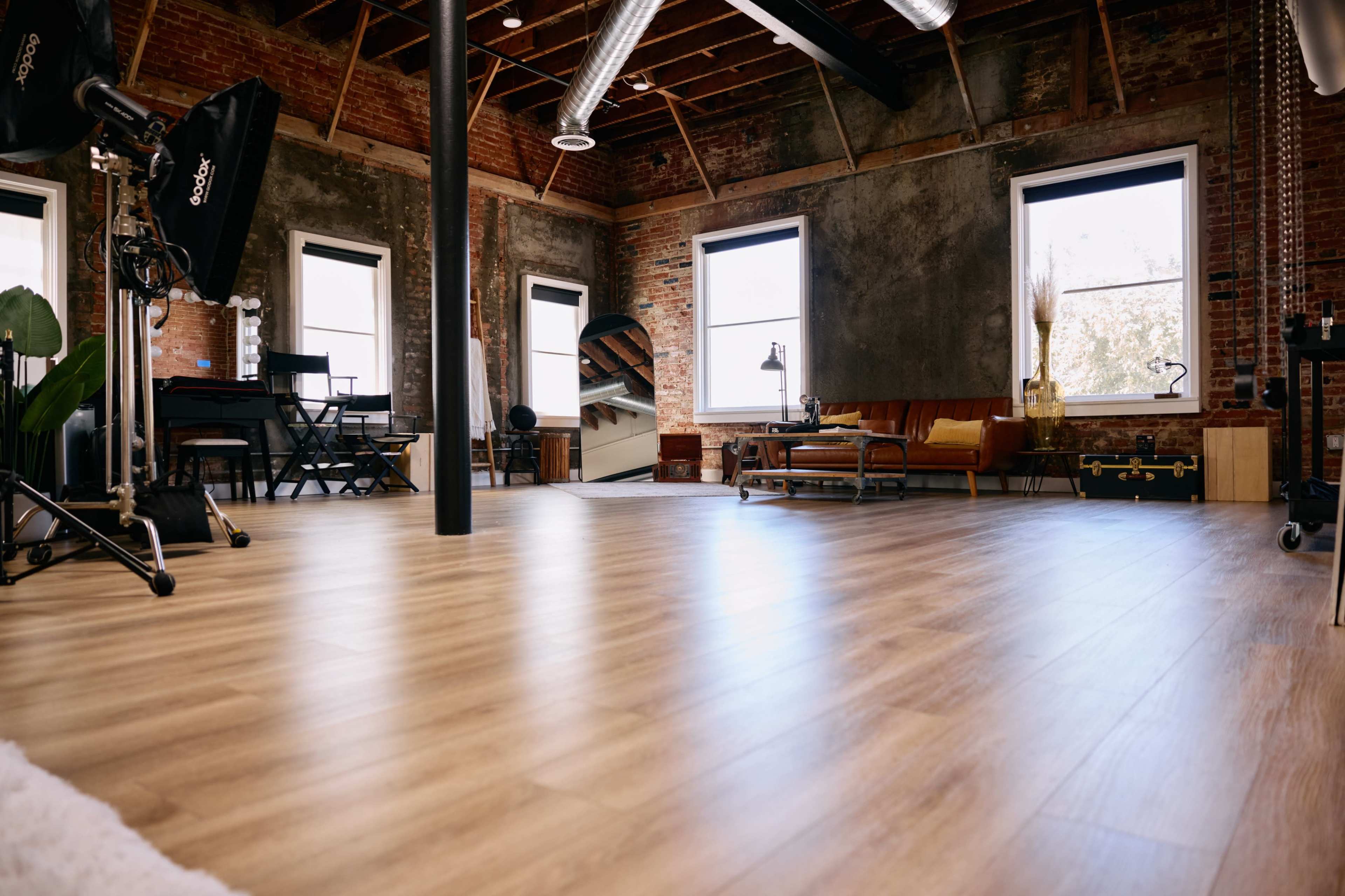 A spacious, retro-style studio with large windows, wooden flooring, and various furniture pieces, including a couch and a workspace.