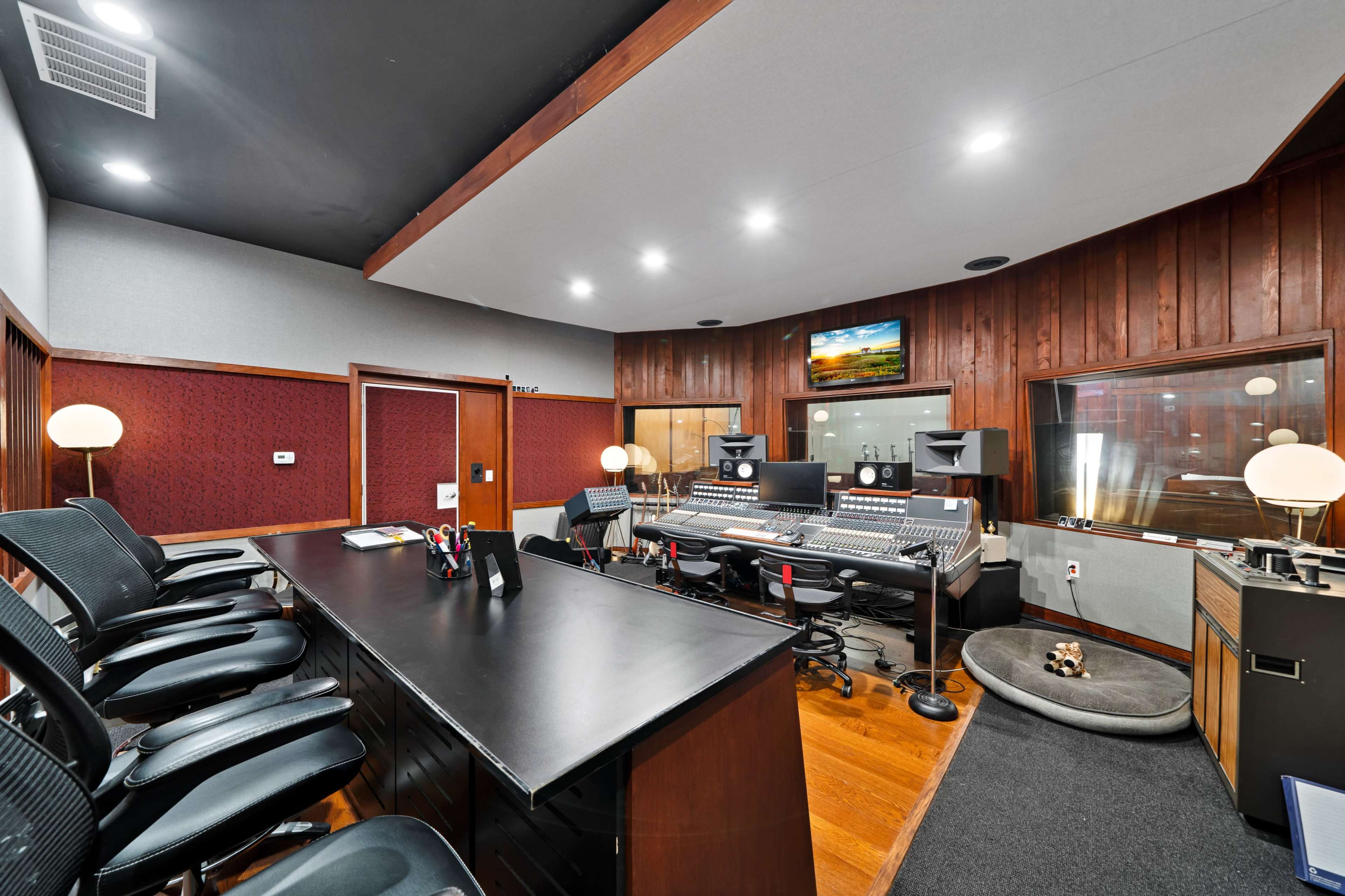A recording studio with checkered seating, mixing equipment, and soundproof glass panels.