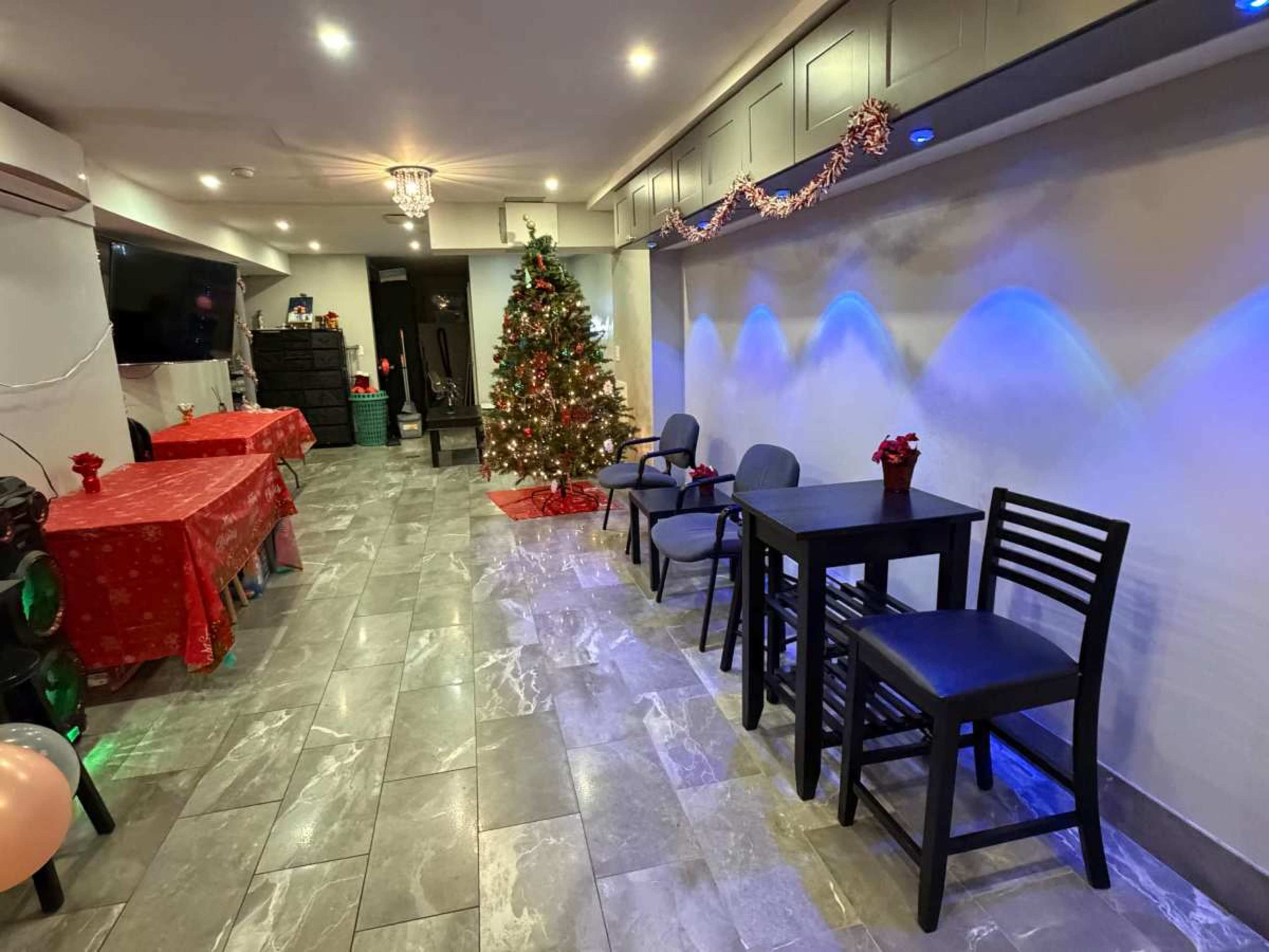 The image shows a decorated room featuring a Christmas tree, tables covered in red tablecloths, and blue lighting along the walls.