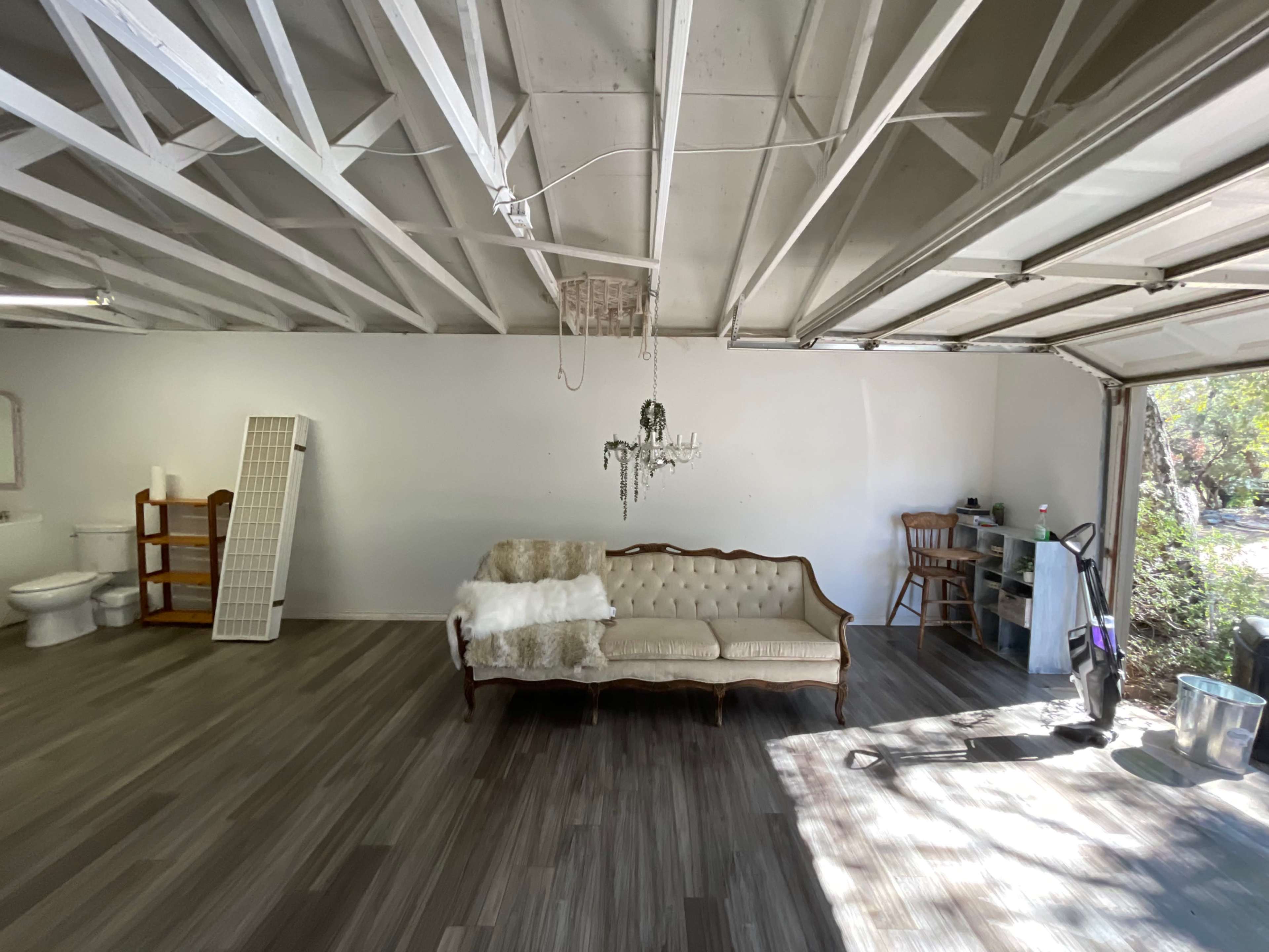 A bare garage features a couch, a toilet, a chandelier, and various pieces of furniture against white walls.